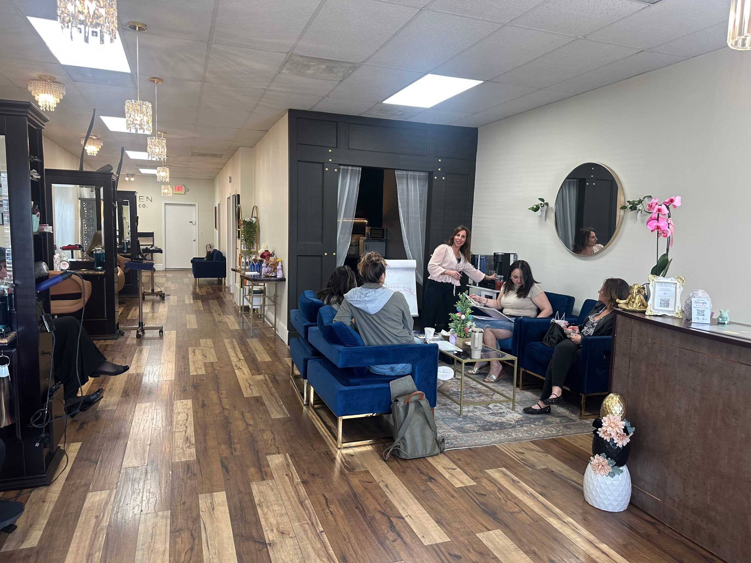 People sitting on blue sofas and chairs in a cozy, well-lit lounge area with wooden flooring and decorative plants.