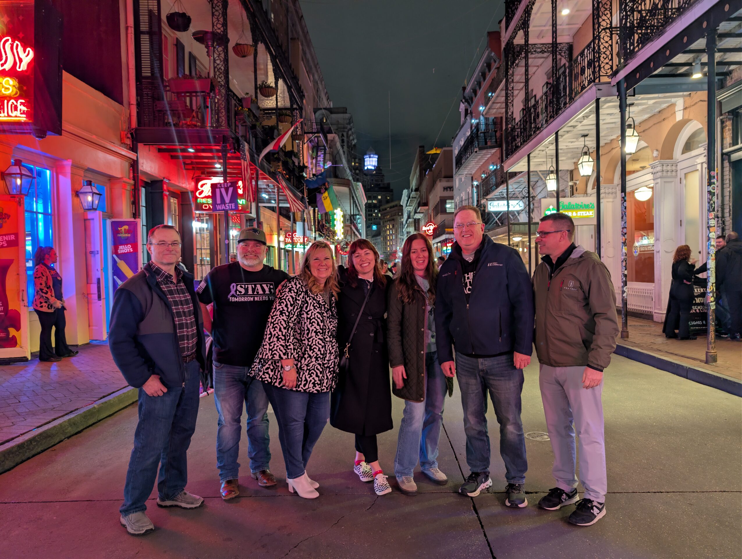 Group of seven people standing on a city street at night, with buildings and lights in the background.