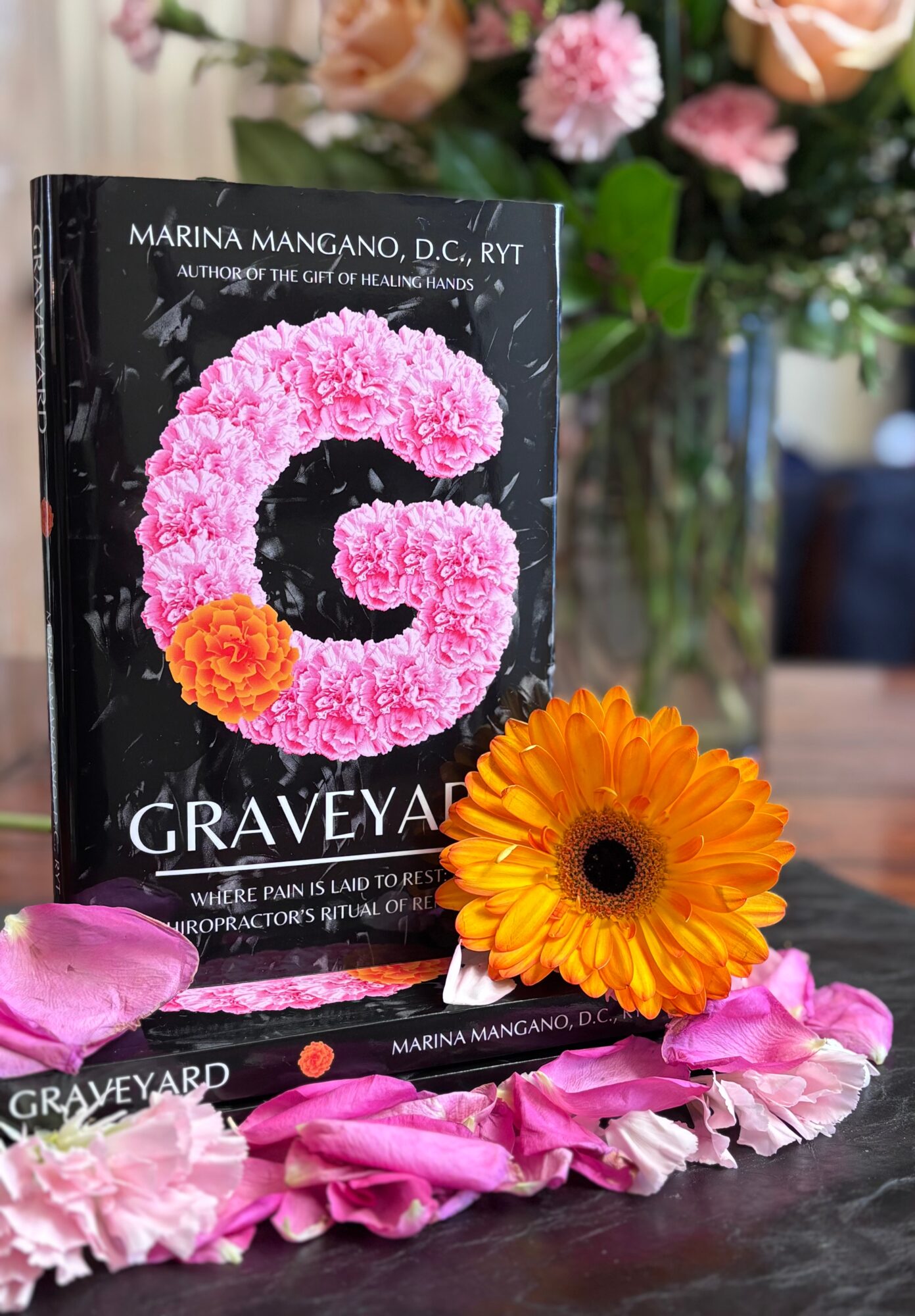 Book titled 'Graveyard' with pink flower design, surrounded by orange and pink flowers on a table.