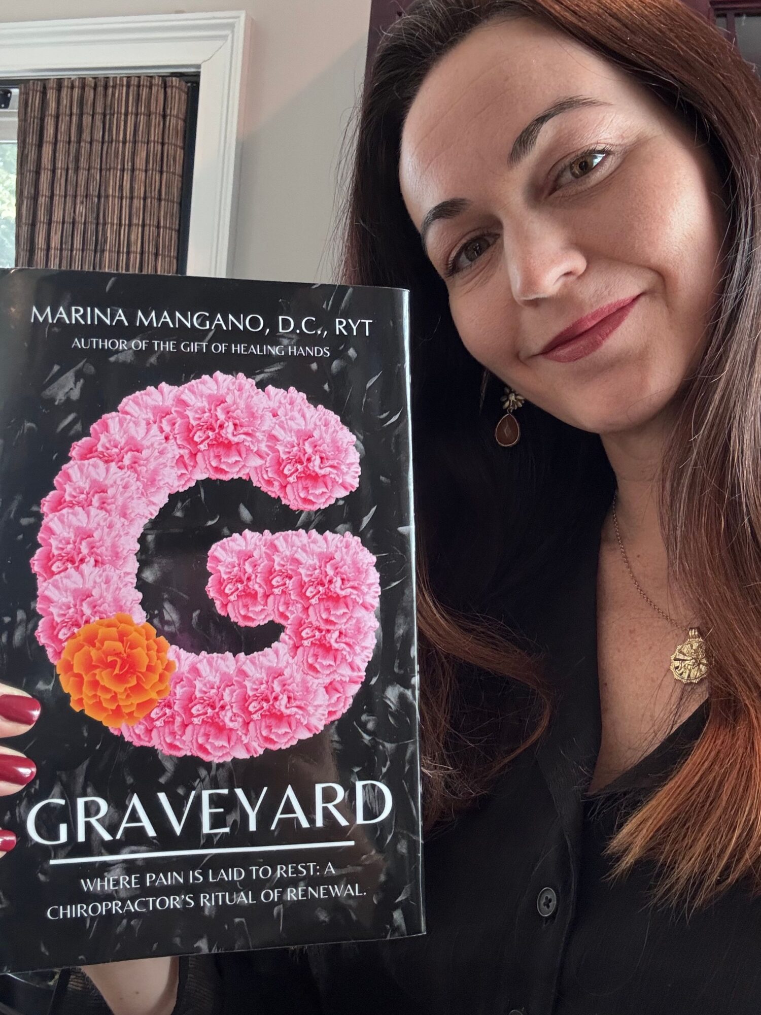 Woman with long brown hair holding a book with a pink and orange floral G on the cover.