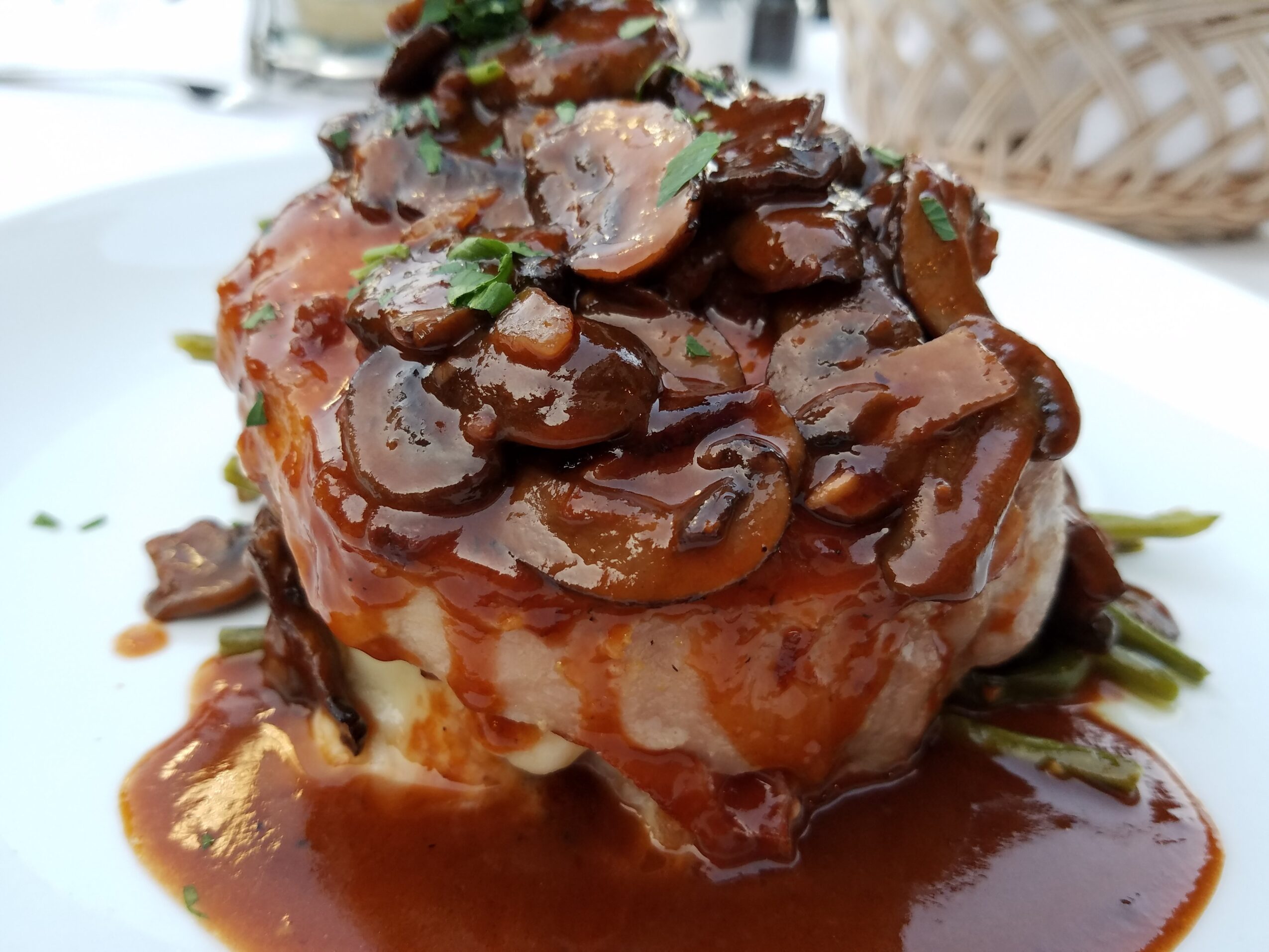A plated dish with a piece of meat topped with mushroom sauce and garnished with herbs.