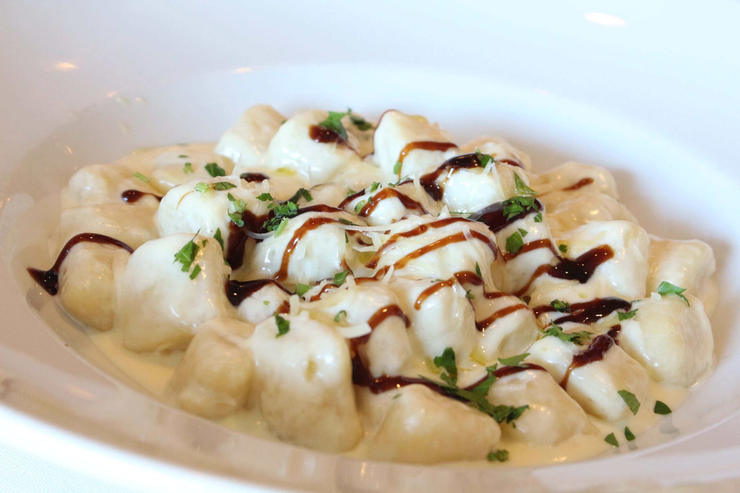 Creamy gnocchi topped with herbs, drizzled with balsamic glaze, served in a white bowl.