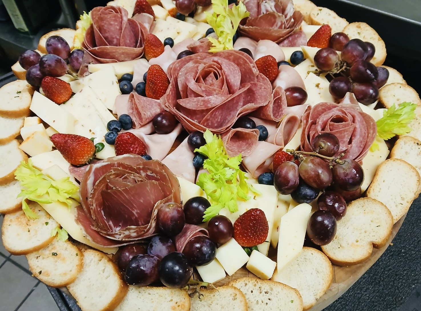 Decorative fruit and cheese platter with grapes, strawberries, cheese slices, and rose-shaped meat or cheese decorations.