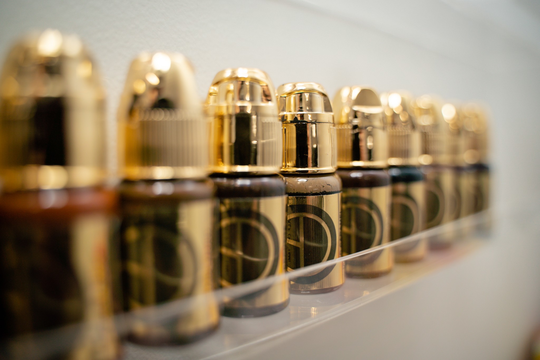 Row of small bottles with gold caps, reflecting on a surface, with a blurred background.