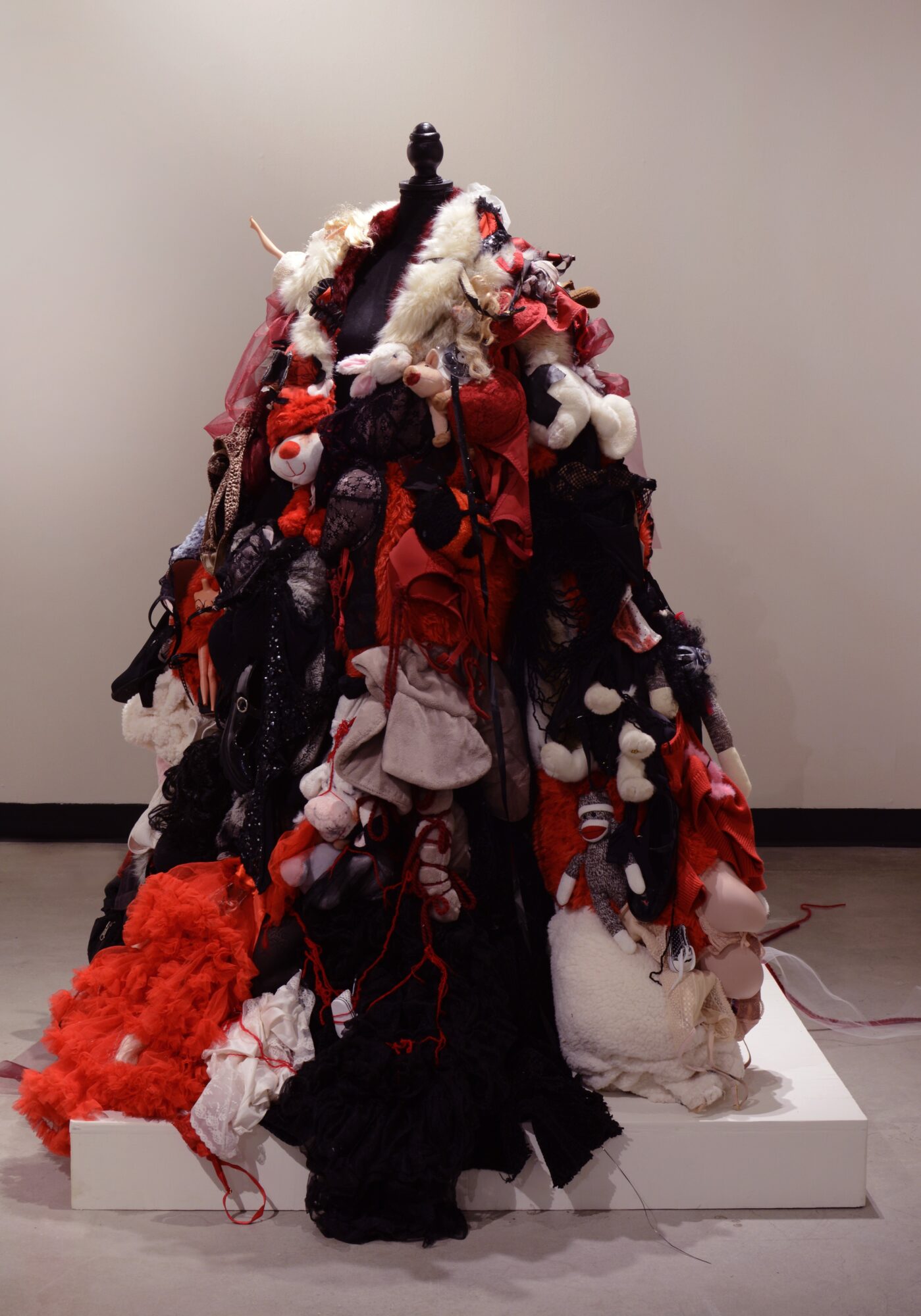 A sculpture made of various fabric and textile materials, resembling a Christmas tree with red, white, black, and gray colors.