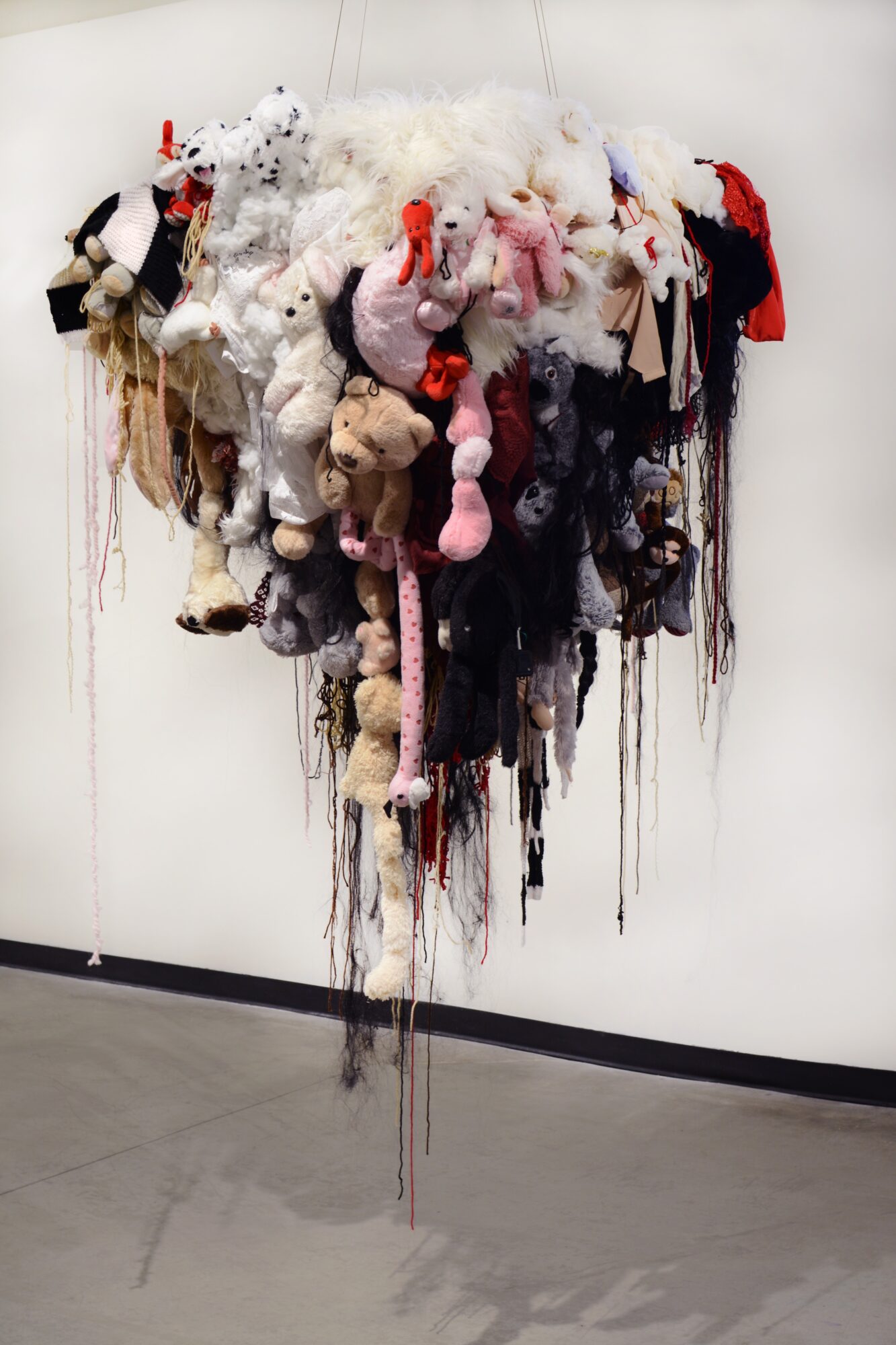 Hanging art installation with various plush toys and fabric items in different colors and textures.