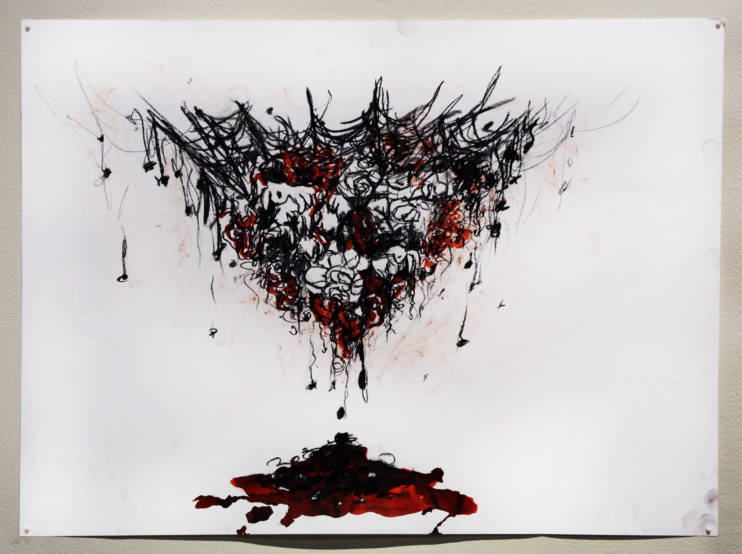 Abstract black and red ink splatter on white background resembling a face or mask with dripping paint.