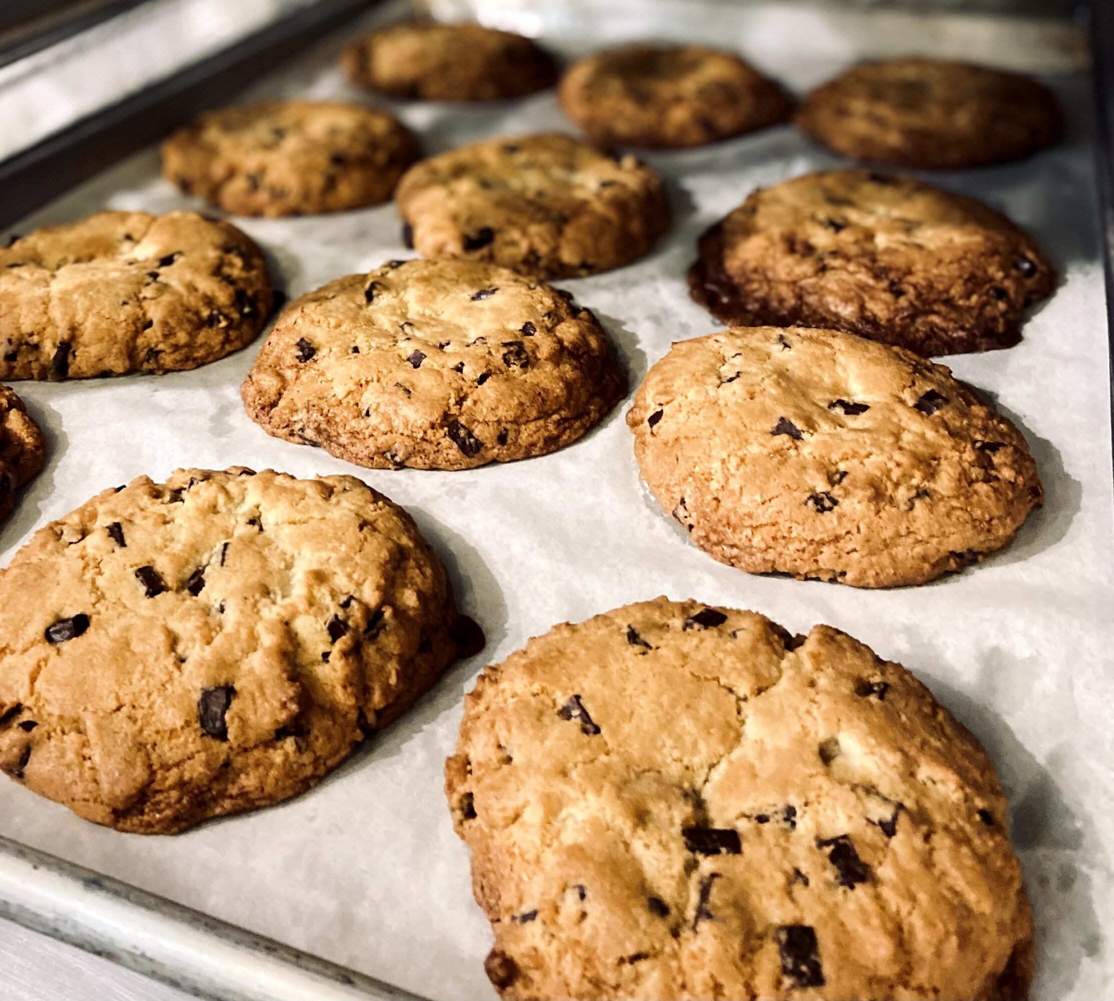 Baked chocolate chip cookies on a baking sheet lined with parchment paper, some with visible chocolate chunks.