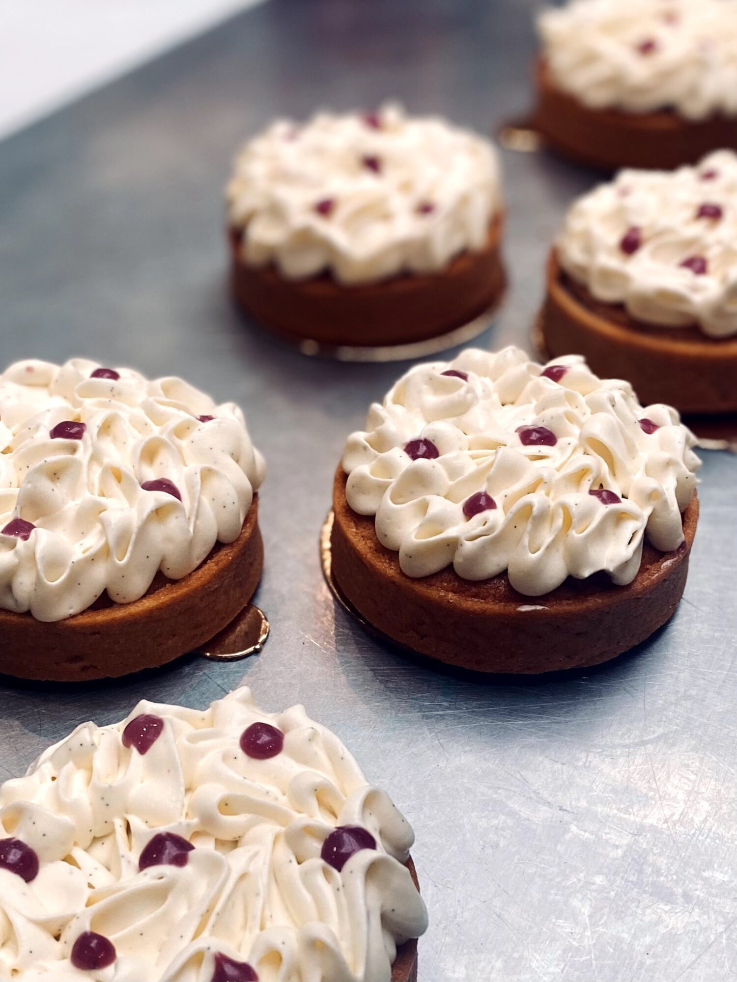 Four cupcakes with white frosting and small purple toppings on a metallic surface.