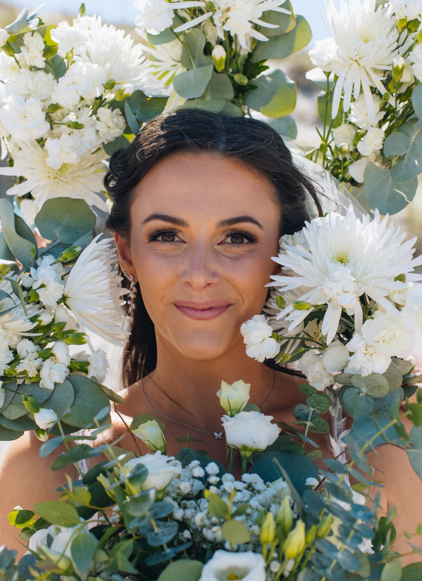Woman with dark hair smiling surrounded by white flowers and greenery.
