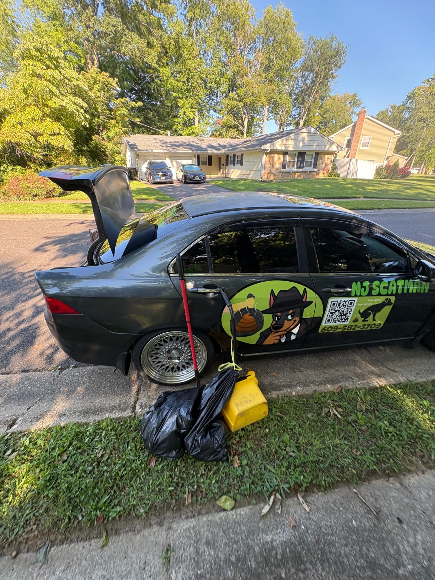 Black vehicle with a yellow and black sign on the side, parked on a street with trees and houses in the background.
