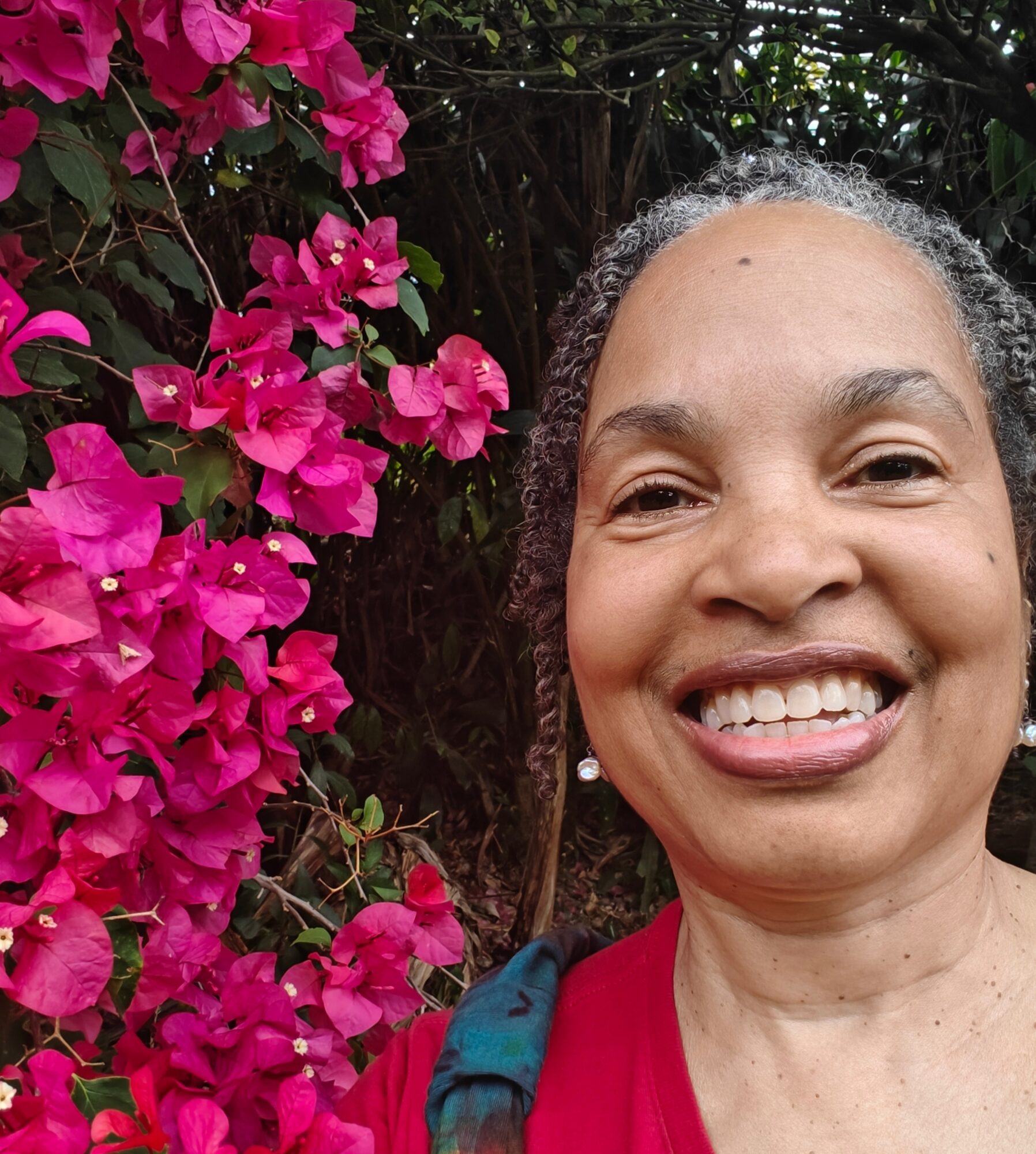 Smiling woman with curly hair in front of pink flowers and greenery.