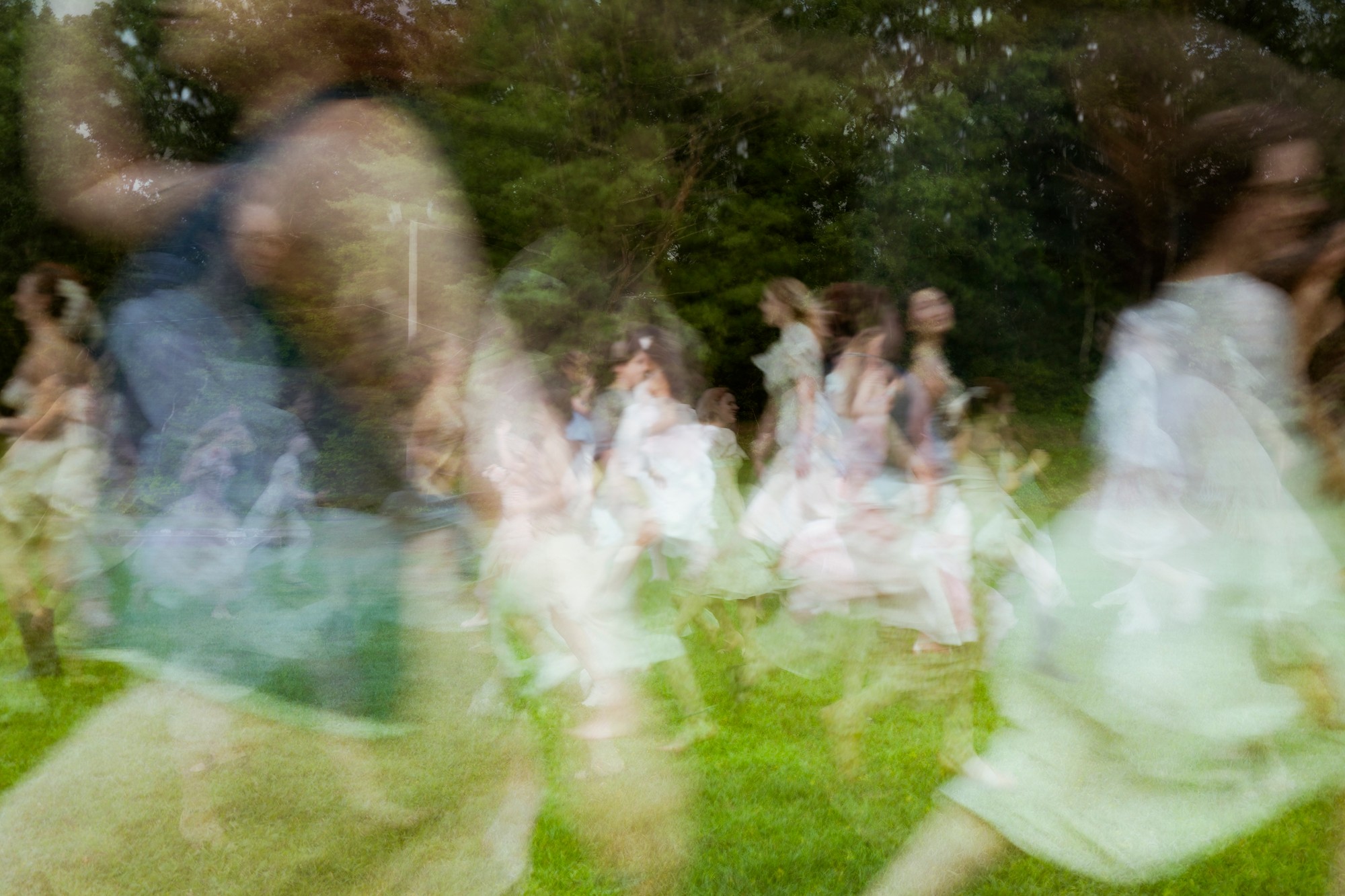 Blurred group of people outdoors, some wearing white, in motion, with trees and grass in background.