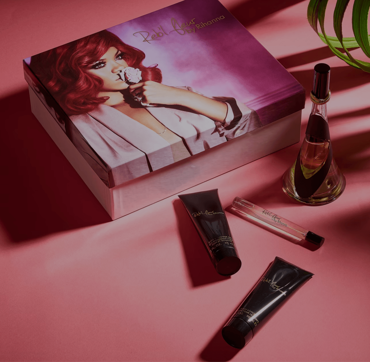 Box with a woman holding a flower, perfume bottle, lipstick, and skincare products on pink surface.