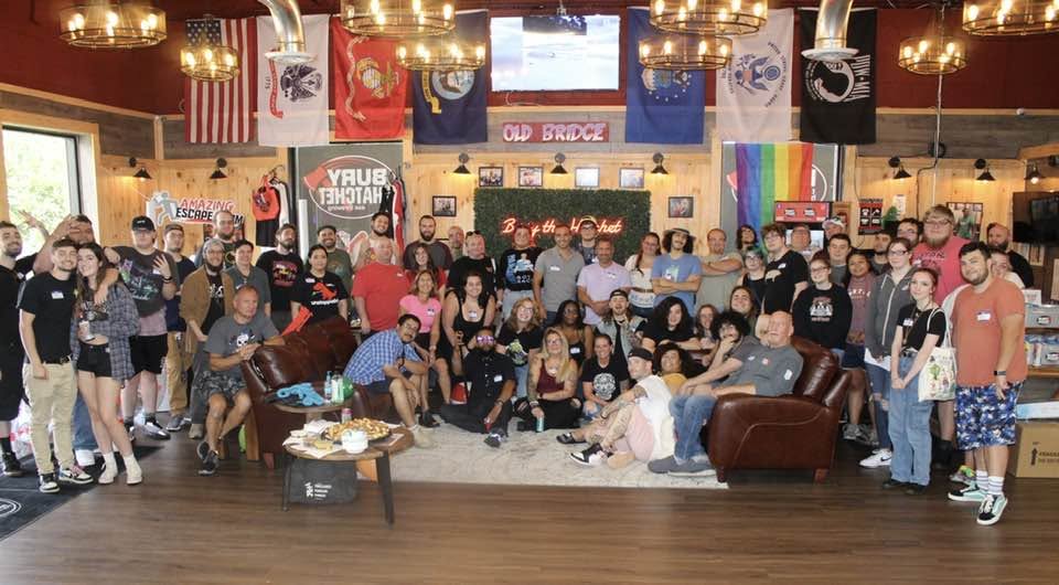 Large group of people gathered in a decorated indoor space with flags and banners, some sitting and others standing.