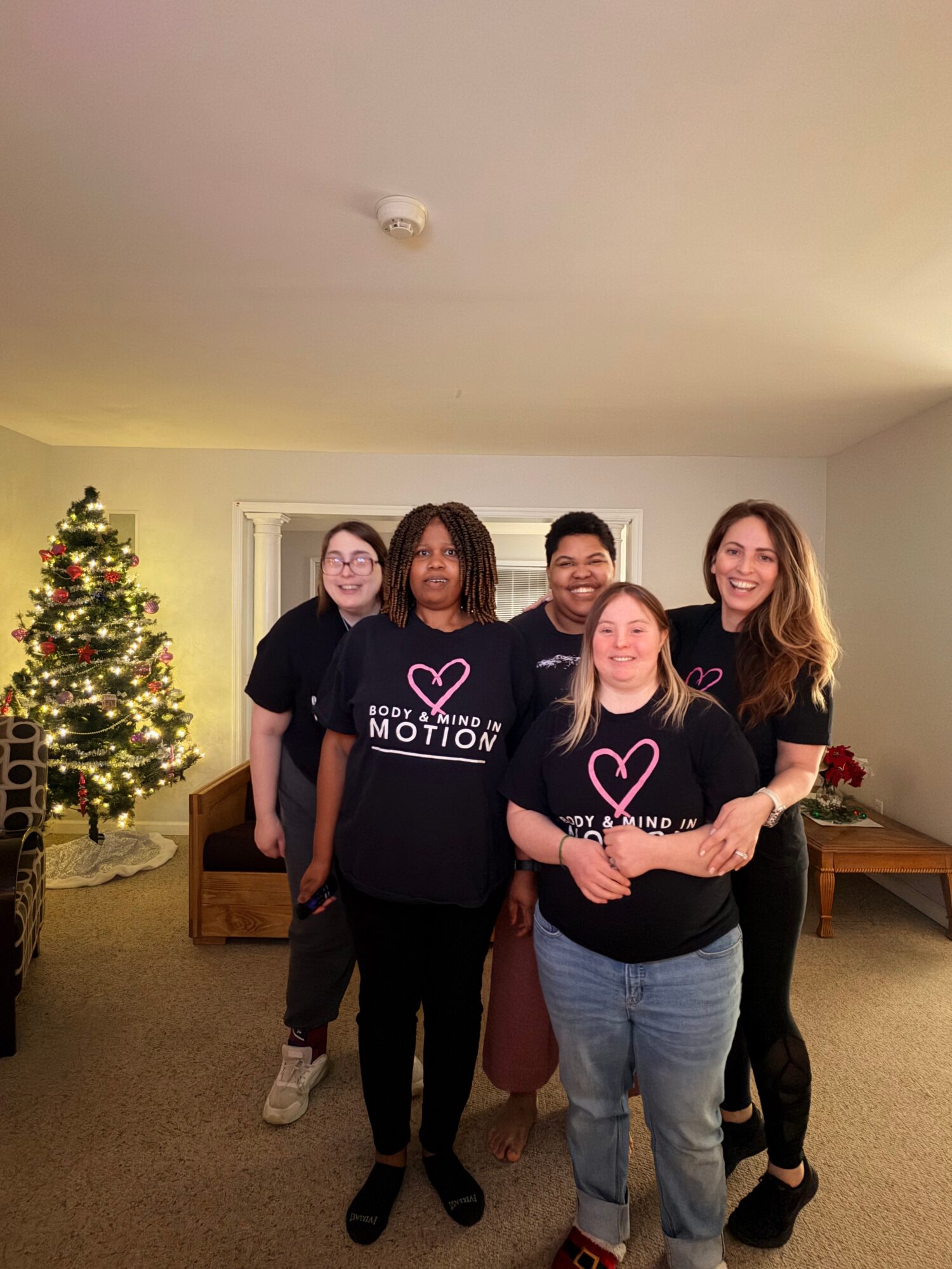 Five people standing in a living room with a decorated Christmas tree, smiling at the camera.
