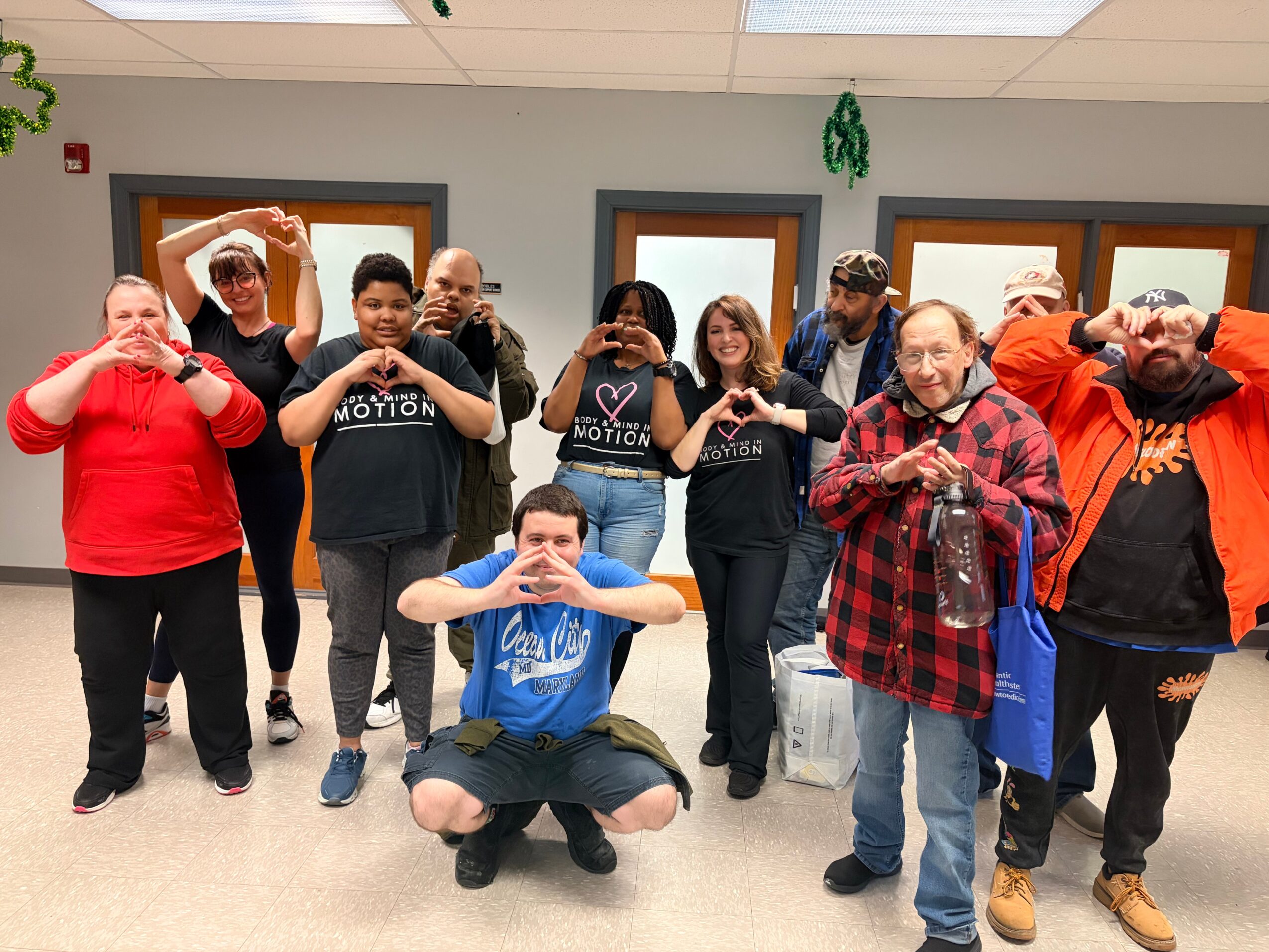 Group of ten people standing indoors, some making heart shapes with their hands, smiling, and posing for the photo.