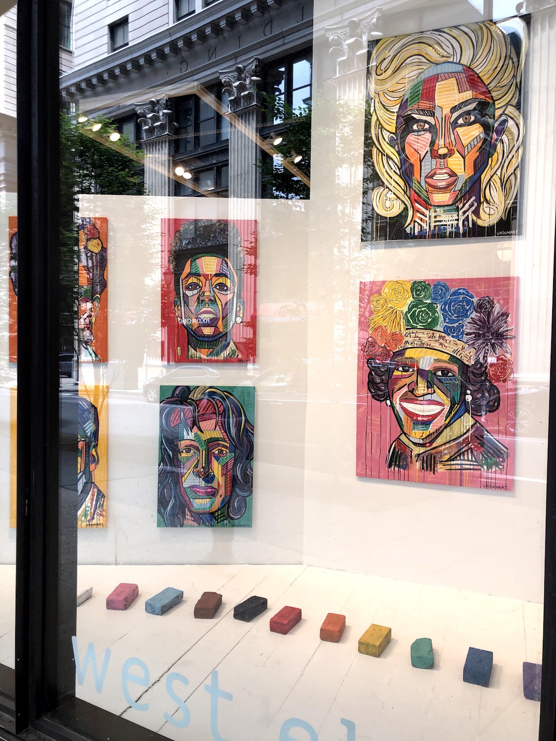 Display window with colorful portraits of women and a row of colored chalks on a white surface.