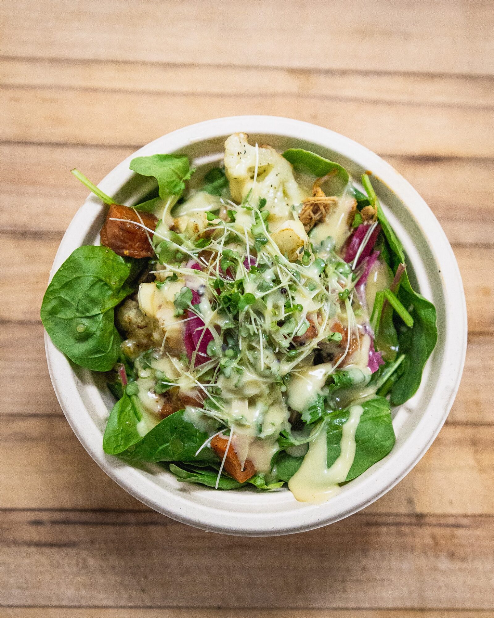 Bowl of mixed salad with greens, vegetables, and sprouts on a wooden surface.