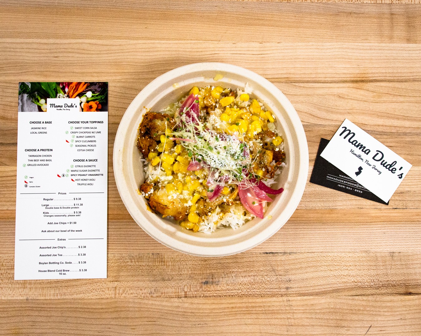 Bowl of salad with yellow toppings, red onions, and shredded cheese on a wooden table, with a menu and a business card nearby.