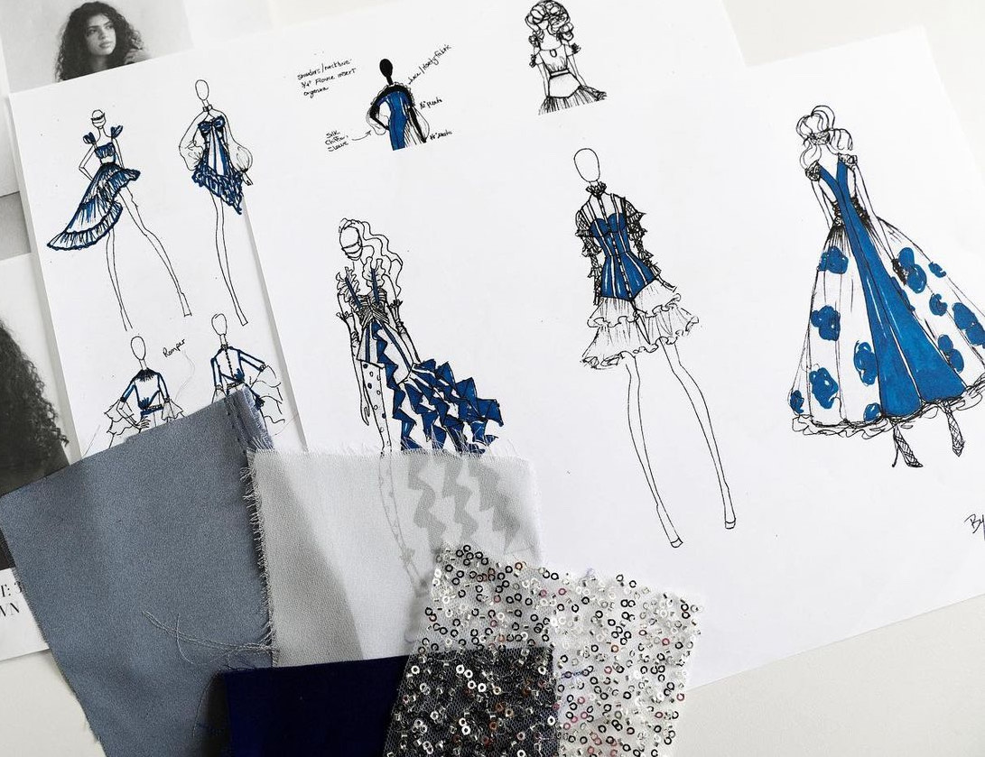 Fashion sketches of dresses, fabric swatches, and embellishments on white paper, arranged on a surface.