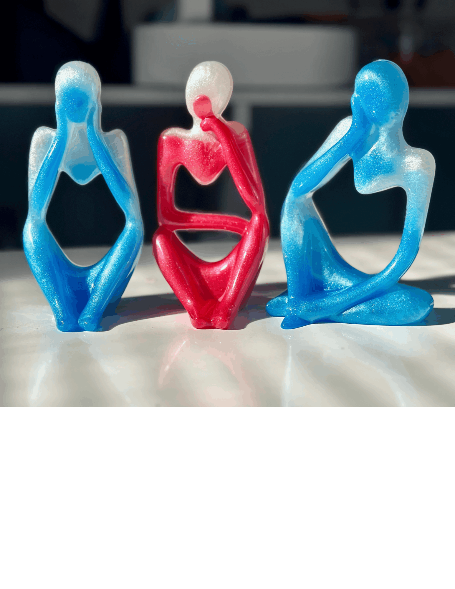 Three abstract sculptures in blue, red, and blue colors, each with a unique pose, on a white surface.