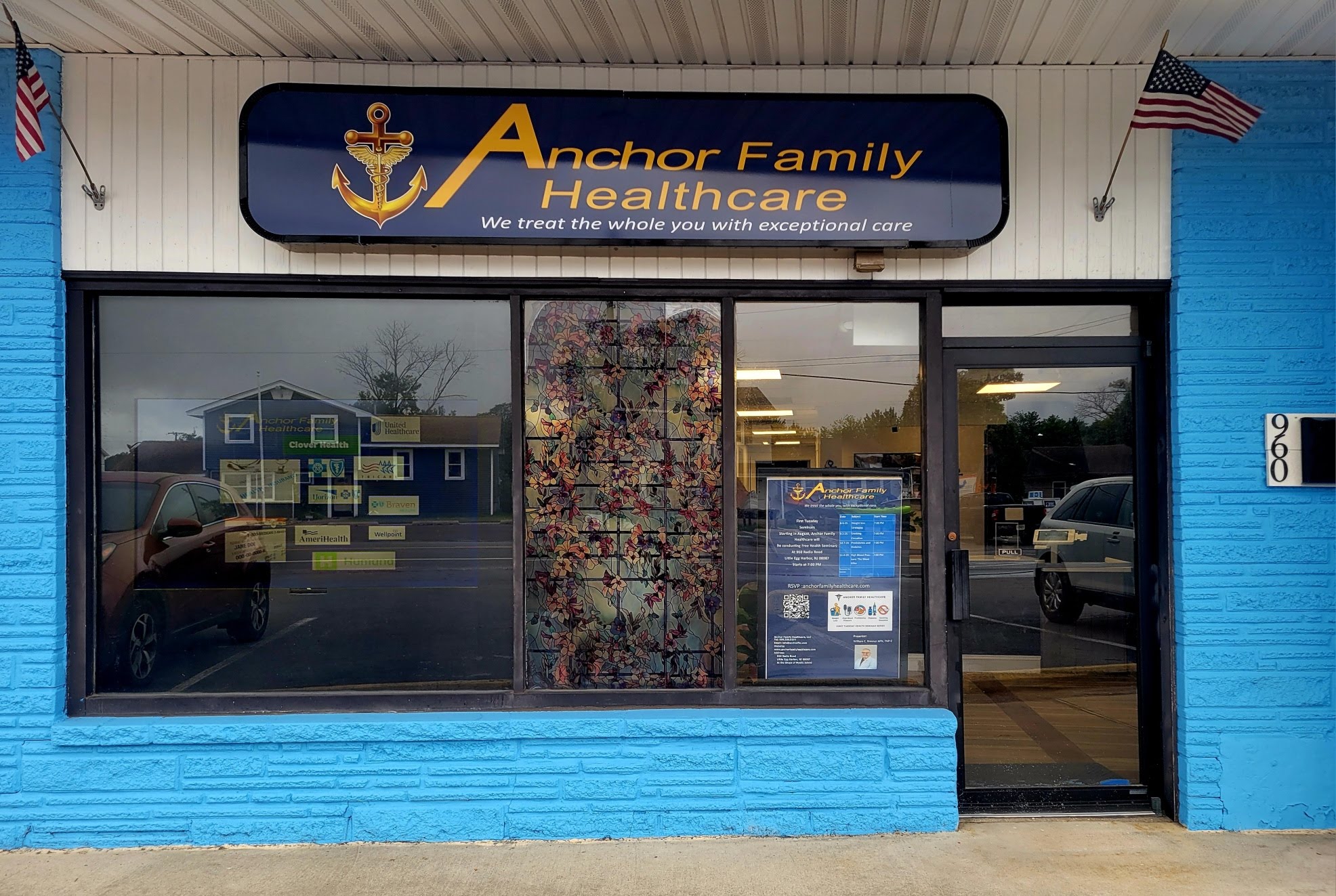 Storefront with a sign reading 'Anchor Family Healthcare' and large glass windows, blue exterior wall, and American flags.