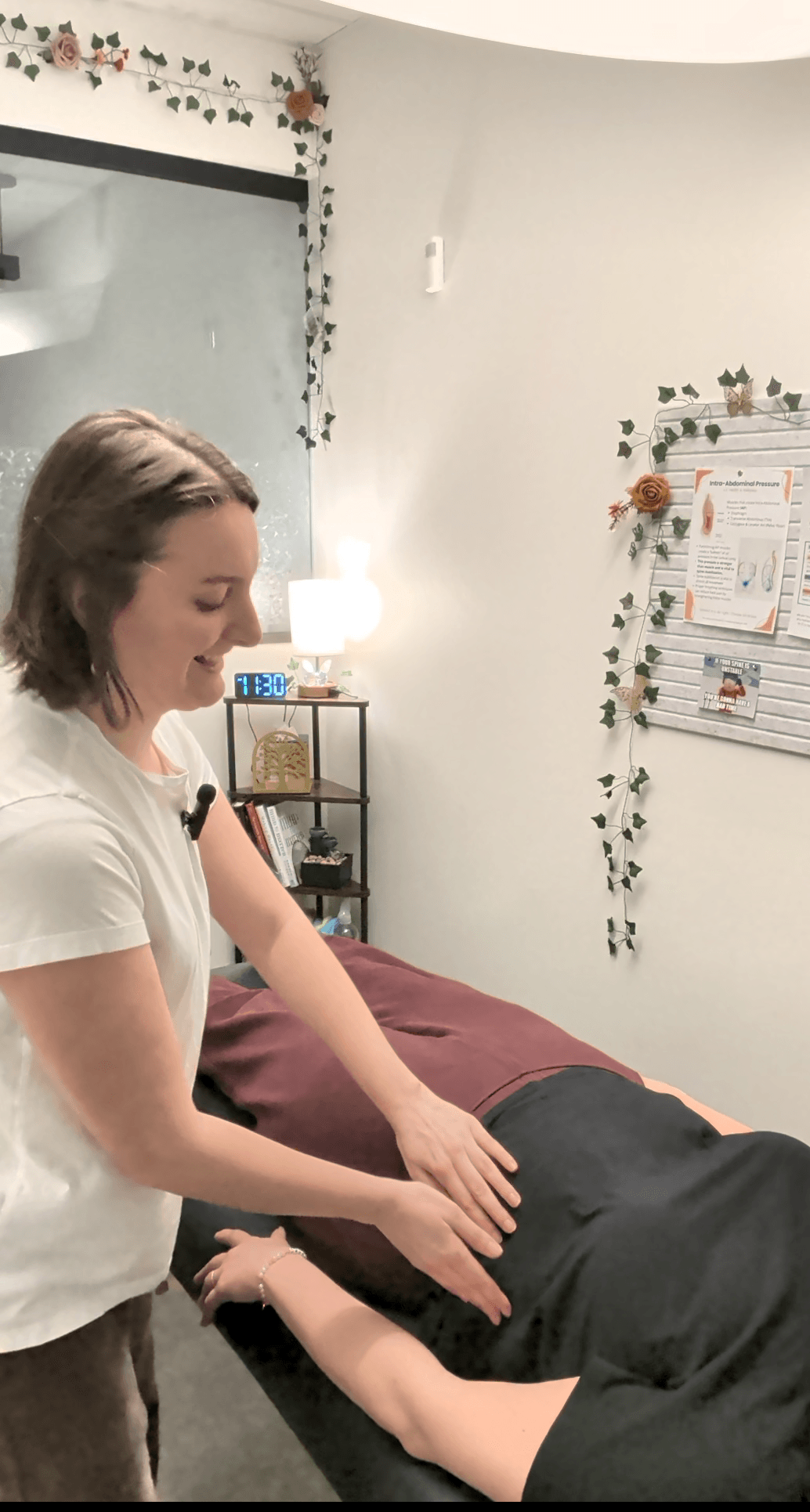 Person receiving a massage on their arm in a room with white walls, a bulletin board, and decorative plants.