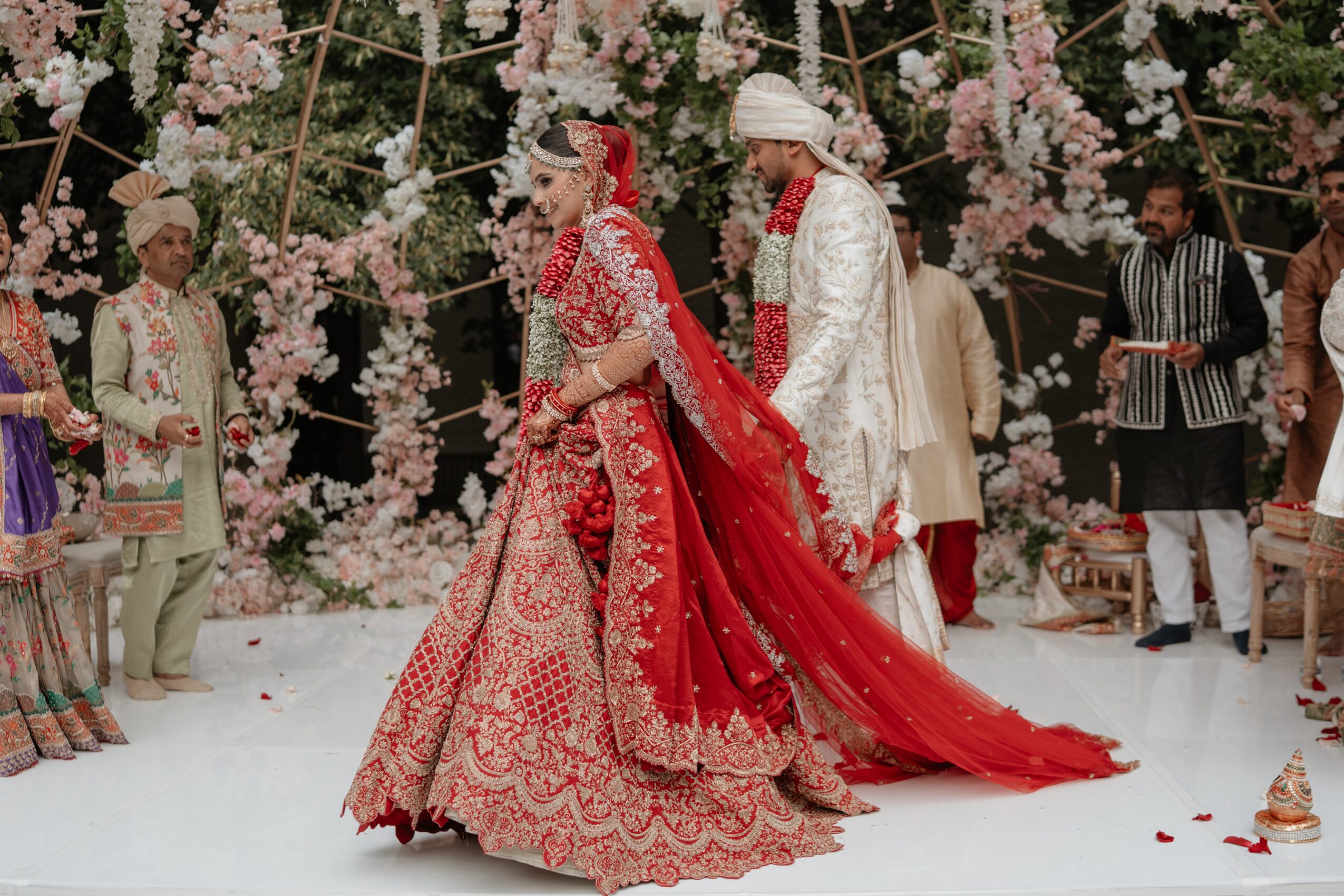 People in traditional attire participate in a wedding ceremony with floral decorations in the background.