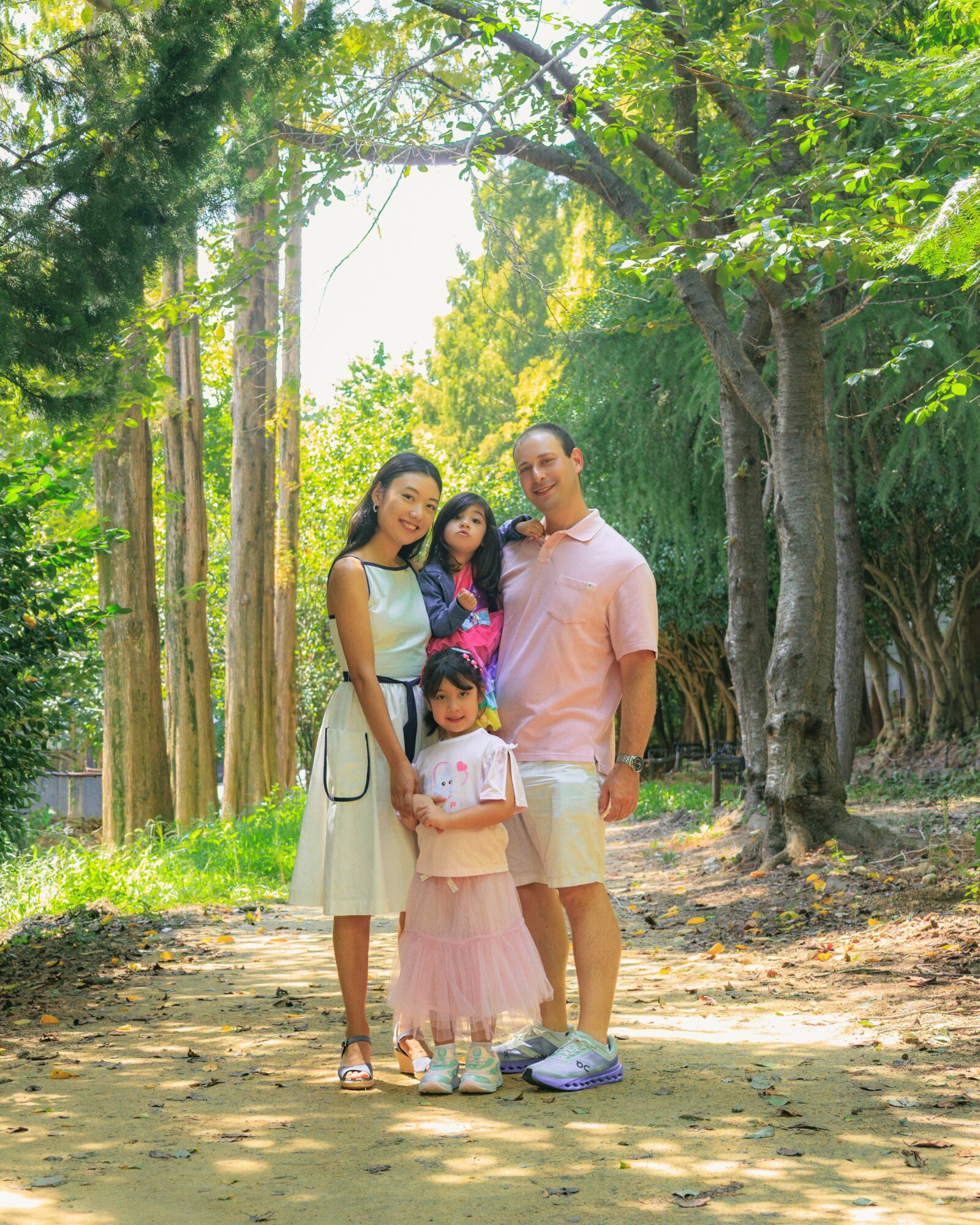Family of four standing on a dirt path surrounded by trees and greenery, smiling outdoors.