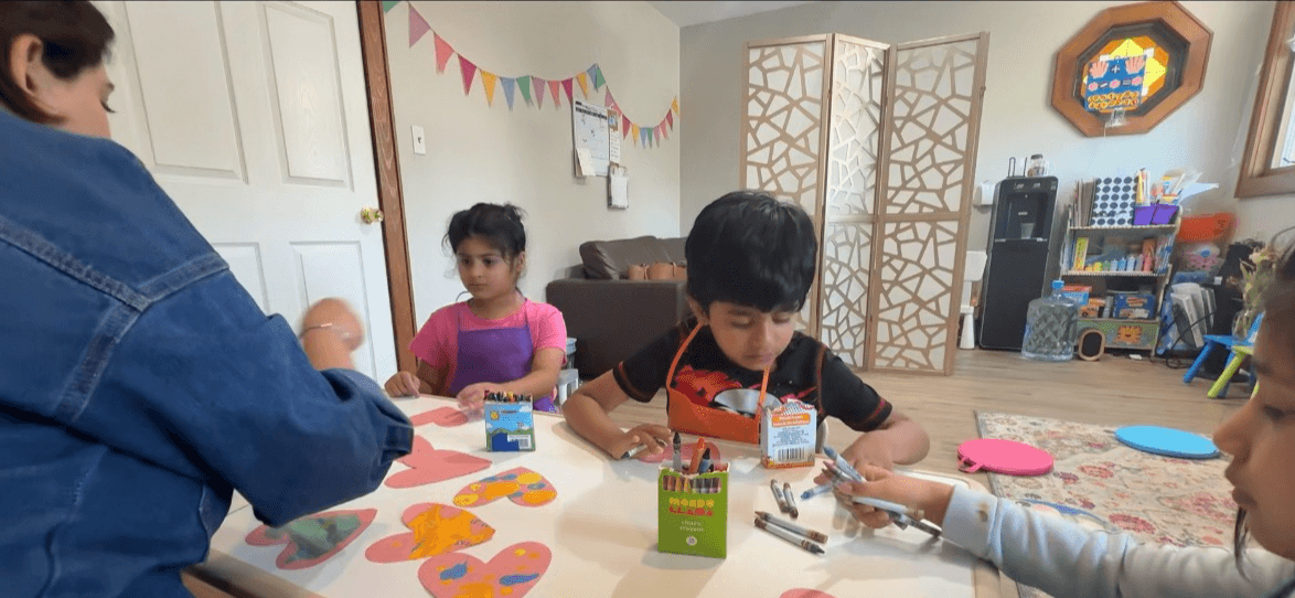 Children and an adult sitting at a table with arts and crafts supplies in a decorated room.