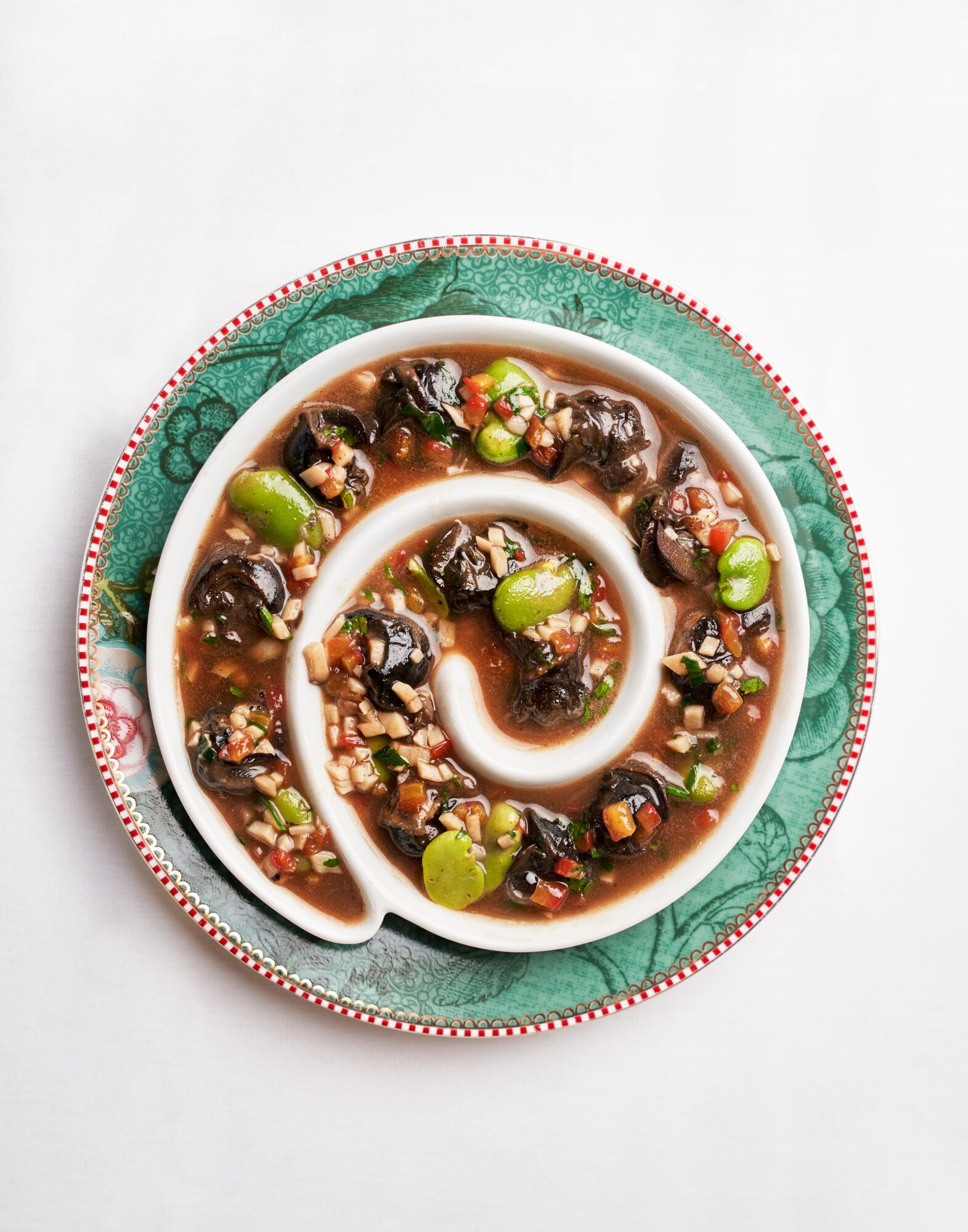 Spiral-shaped dish with dark ingredients and green garnishes on a decorative plate, viewed from above.
