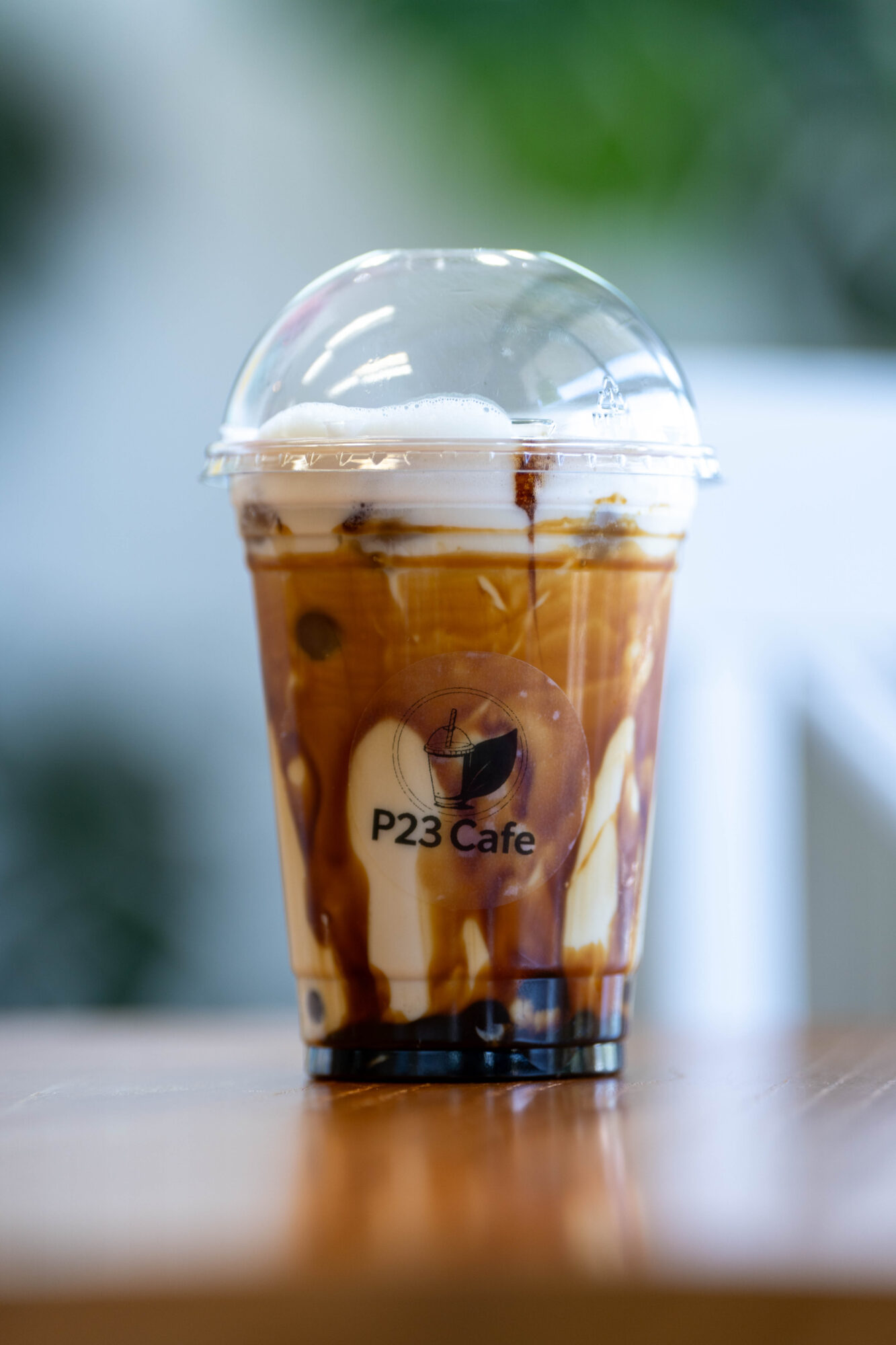 Cold coffee drink with whipped cream in a clear plastic cup on a wooden surface, blurred background.