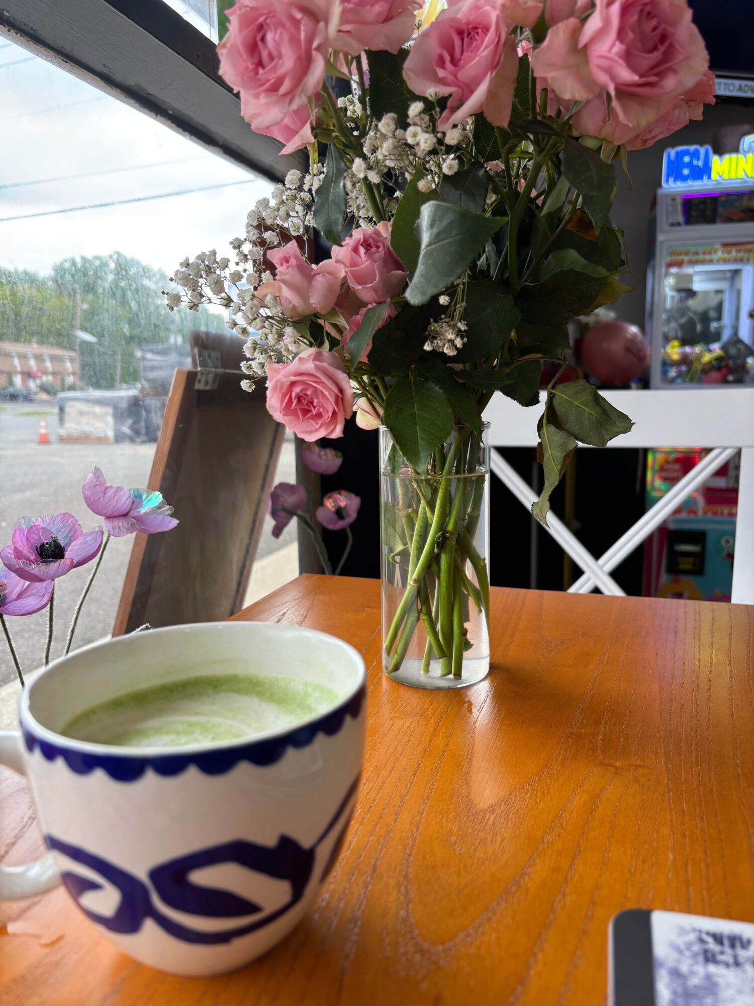Pink roses and white baby's breath in a glass vase on a wooden table, with a cup of green tea nearby.