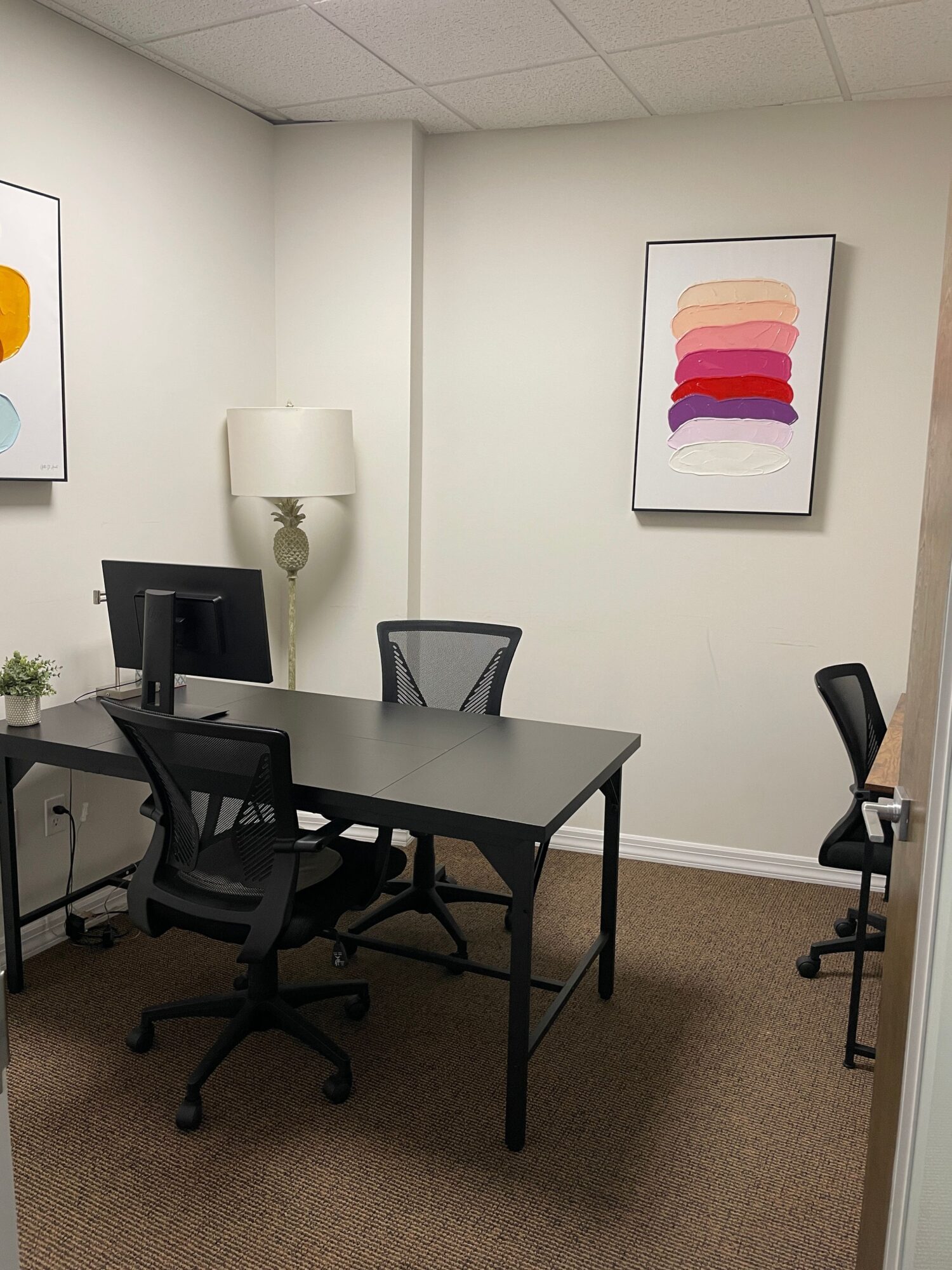 Office with a desk, chair, computer, lamp, and framed colorful artwork on the wall.