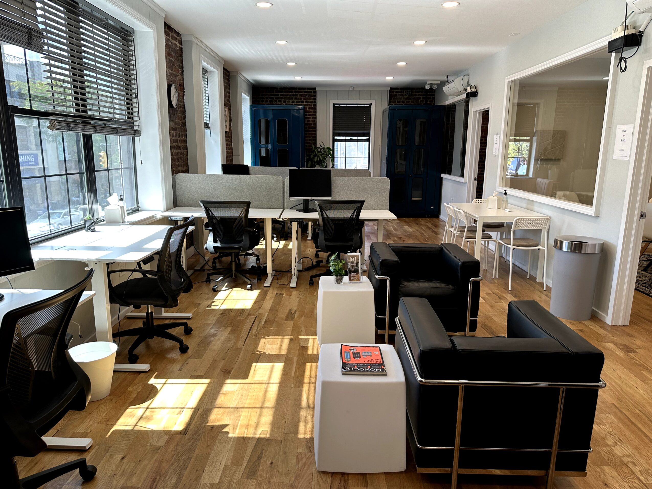 Office space with desks, chairs, a black sofa, and windows letting in sunlight.