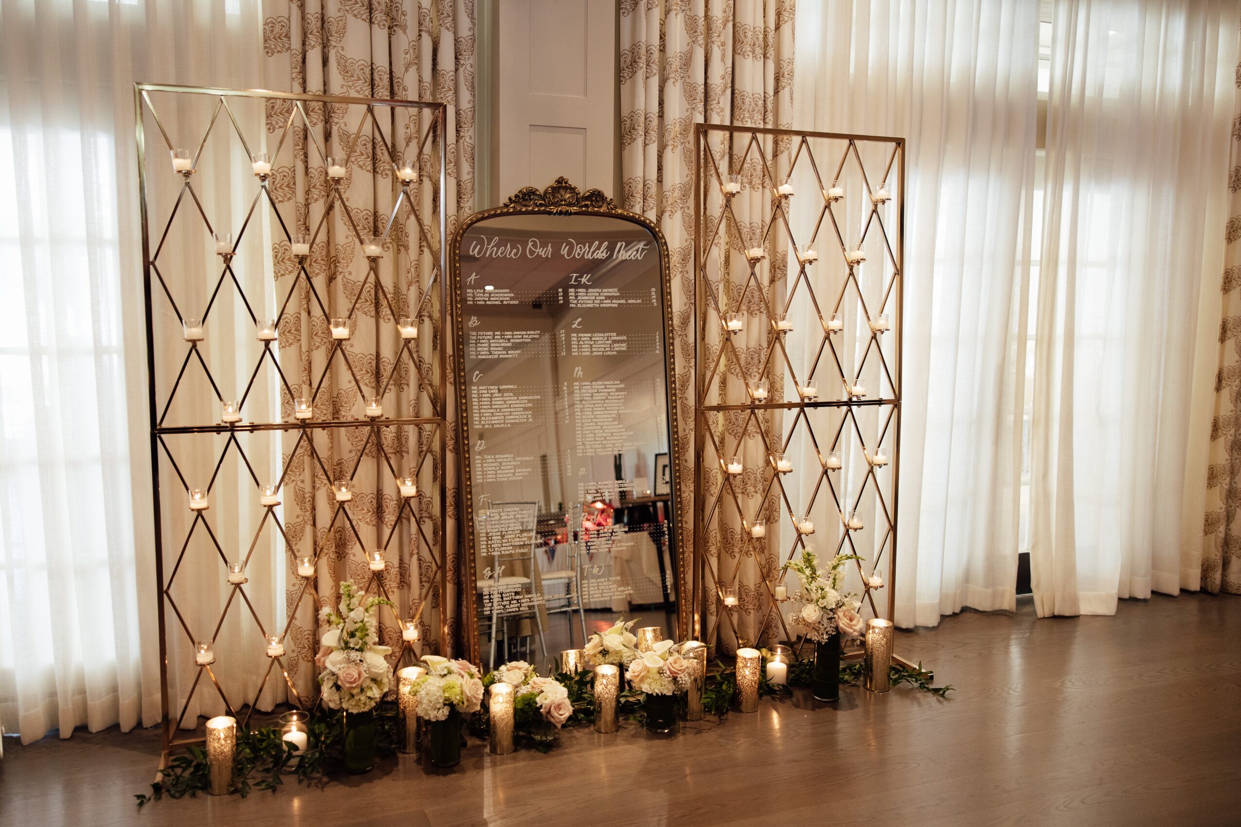 Decorative setup with a large mirror, floral arrangements, and string lights in a room with curtains.