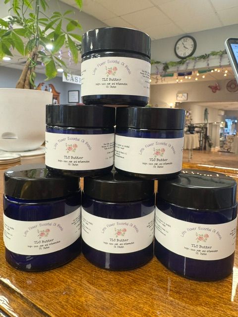 Seven dark blue jars with white labels arranged on a wooden surface, with a plant and a kitchen background visible.