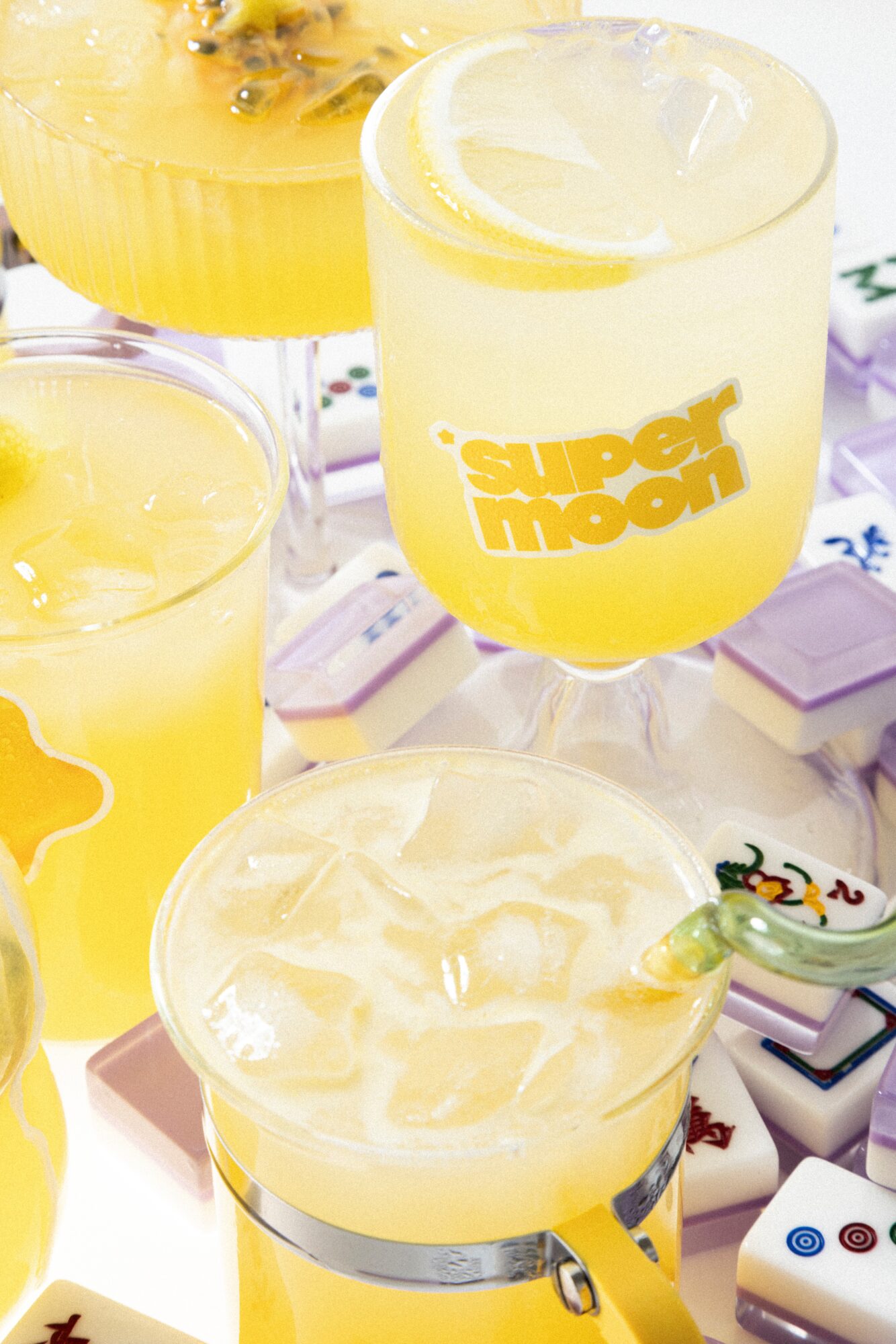Two yellow beverages in glasses with ice, one with lemon slice, and a yellow drink with a straw, on a table.