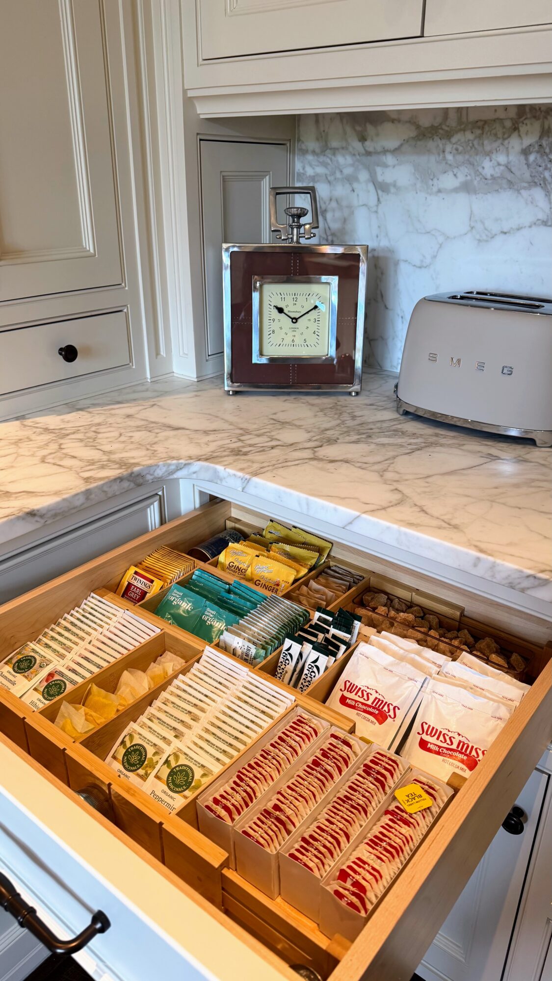 Open drawer with various packaged food items on a kitchen countertop, with a clock and toaster in the background.