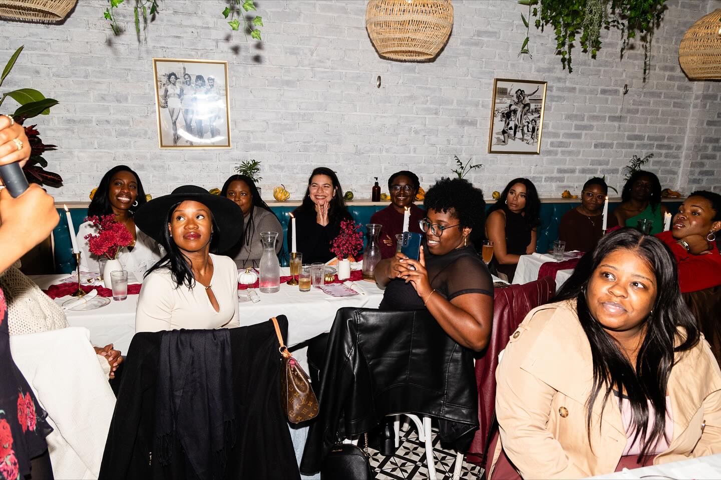 Group of women sitting at a table in a decorated indoor setting, some smiling and looking at a person speaking.