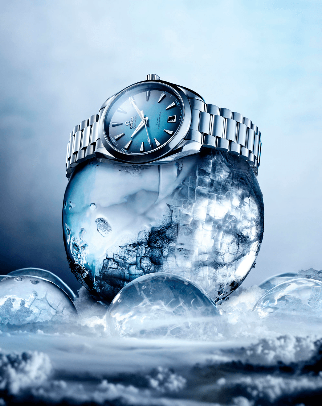 A silver wristwatch resting on a large ice sphere with smaller ice spheres around it, set against a cool blue background.