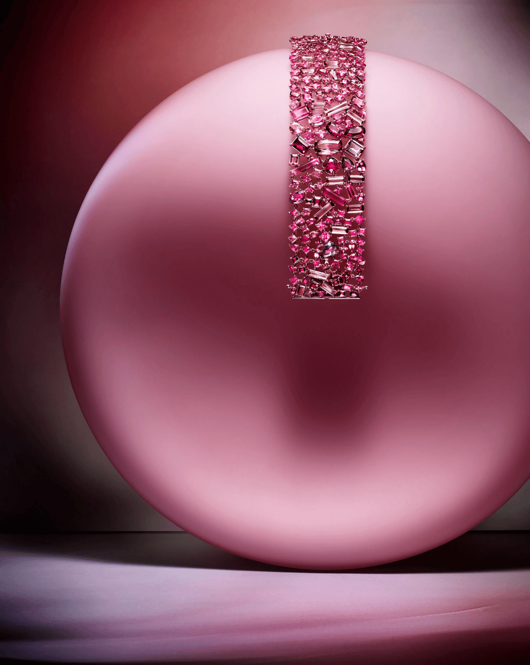 Pink spherical ornament with a vertical strip of pink gemstones or beads, shiny surface, and blurred background.