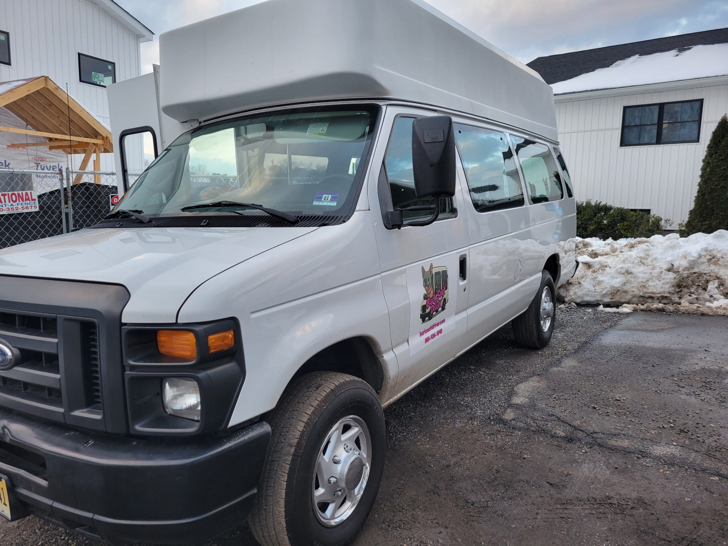 White van parked on a driveway with snow and residential buildings in background.