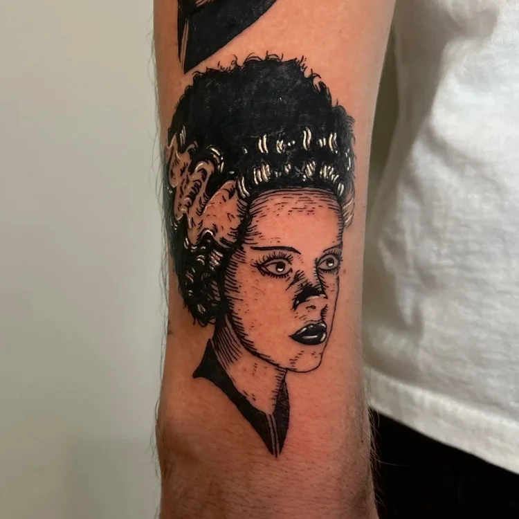 Black and gray tattoo of a woman's face with curly hair on person's arm, detailed shading and line work.