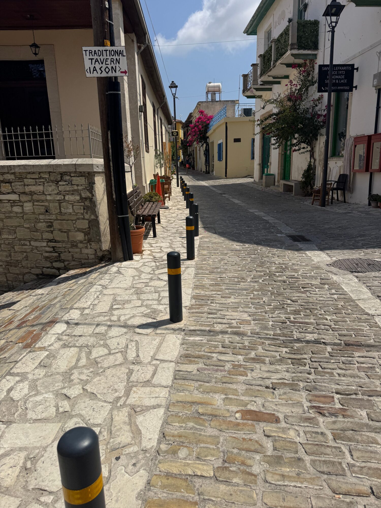 Cobblestone street with buildings, street lamp, and a sign, viewed from a corner, with a partly cloudy sky.