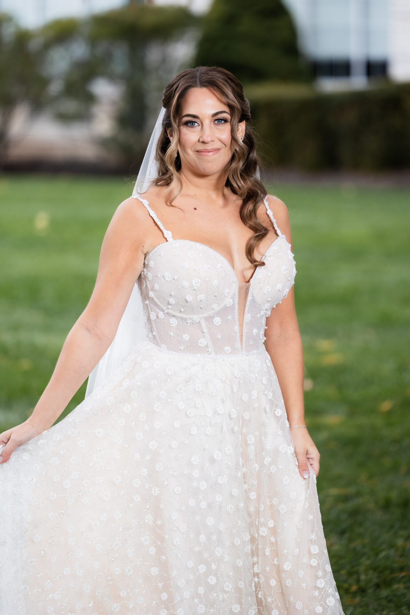 Young woman in wedding dress outdoors, smiling, with trees and grass in background.