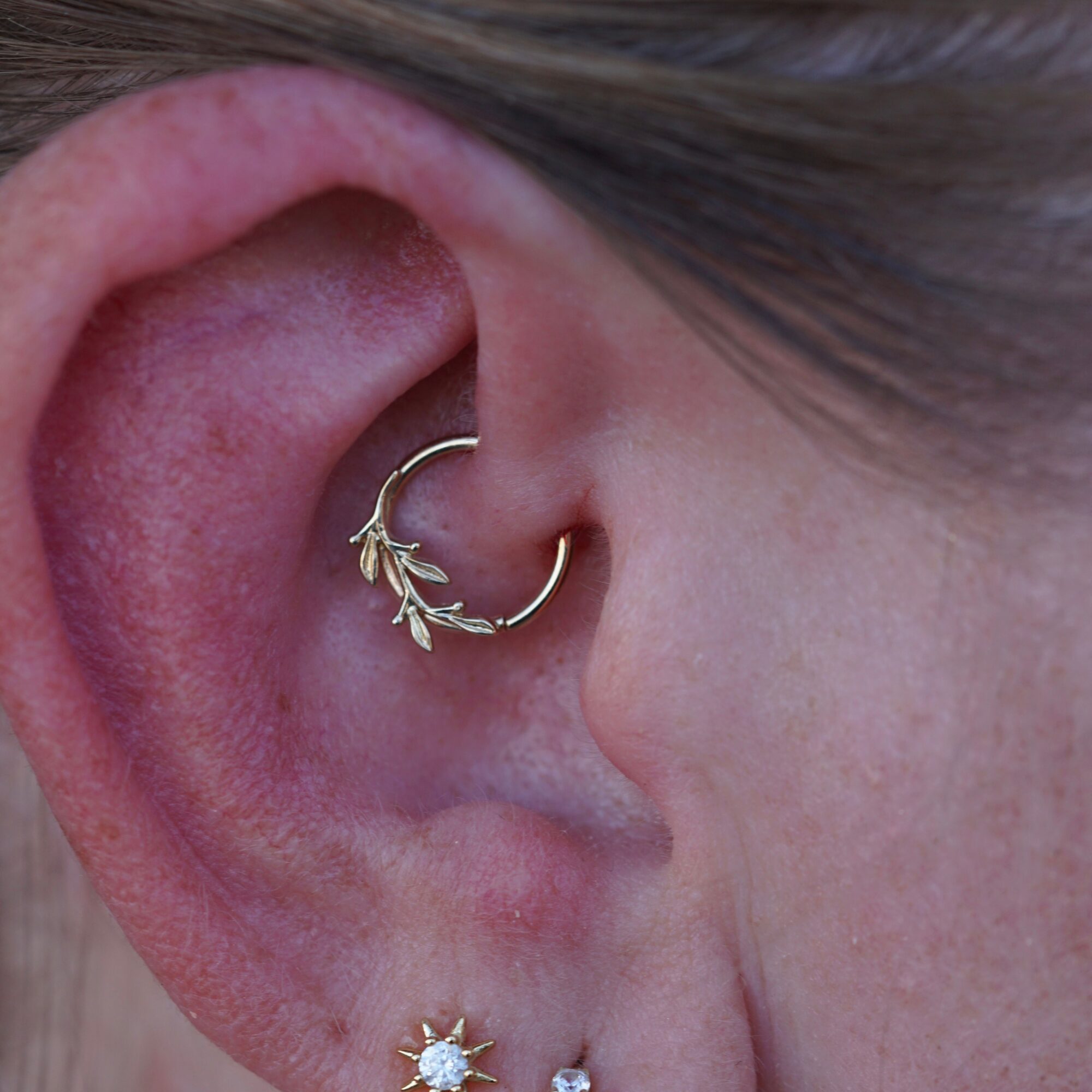 Close-up of a person's ear with a gold hoop and a decorative earring with a white gemstone.