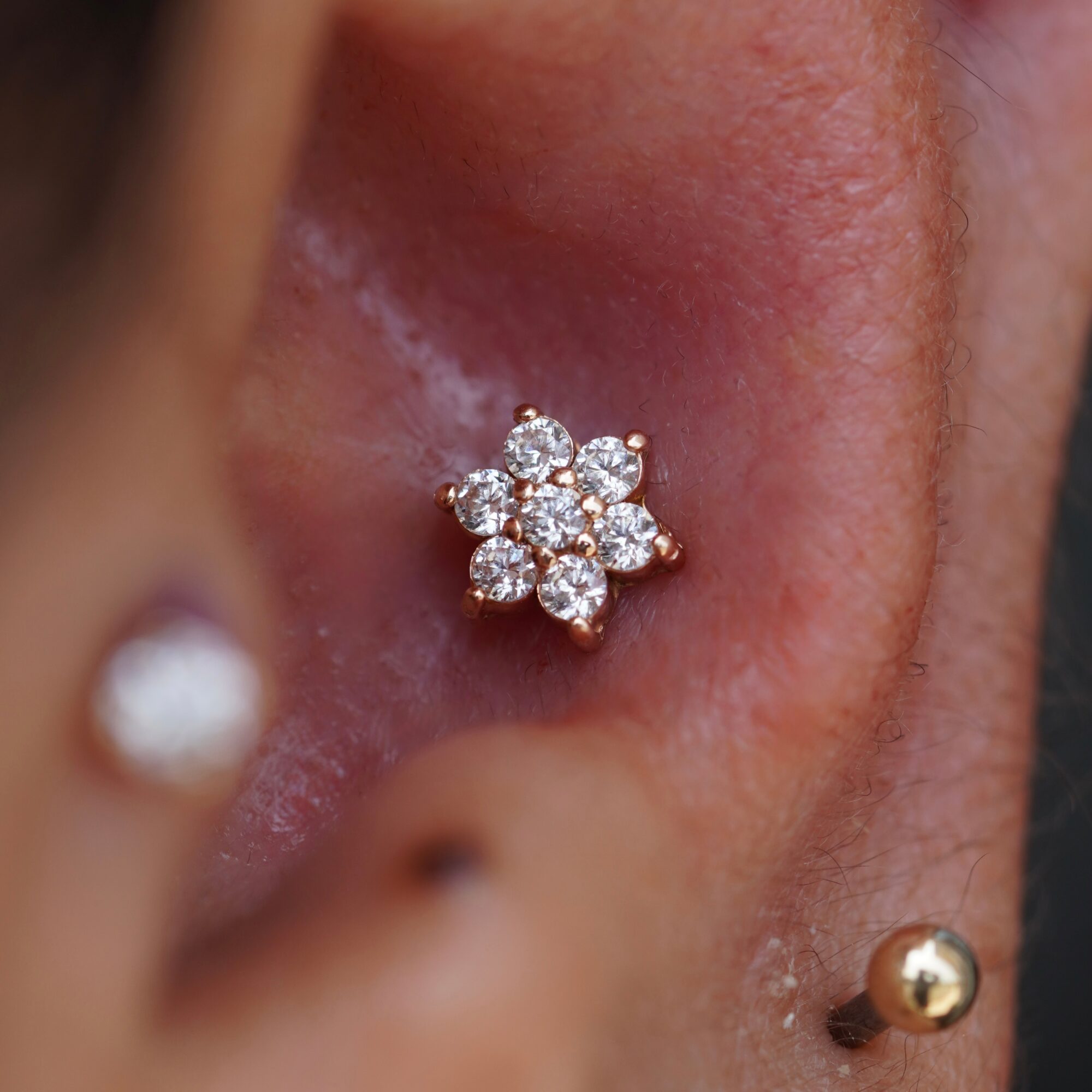 Close-up of a person's ear with a flower-shaped diamond stud earring and a gold ball earring, skin visible.