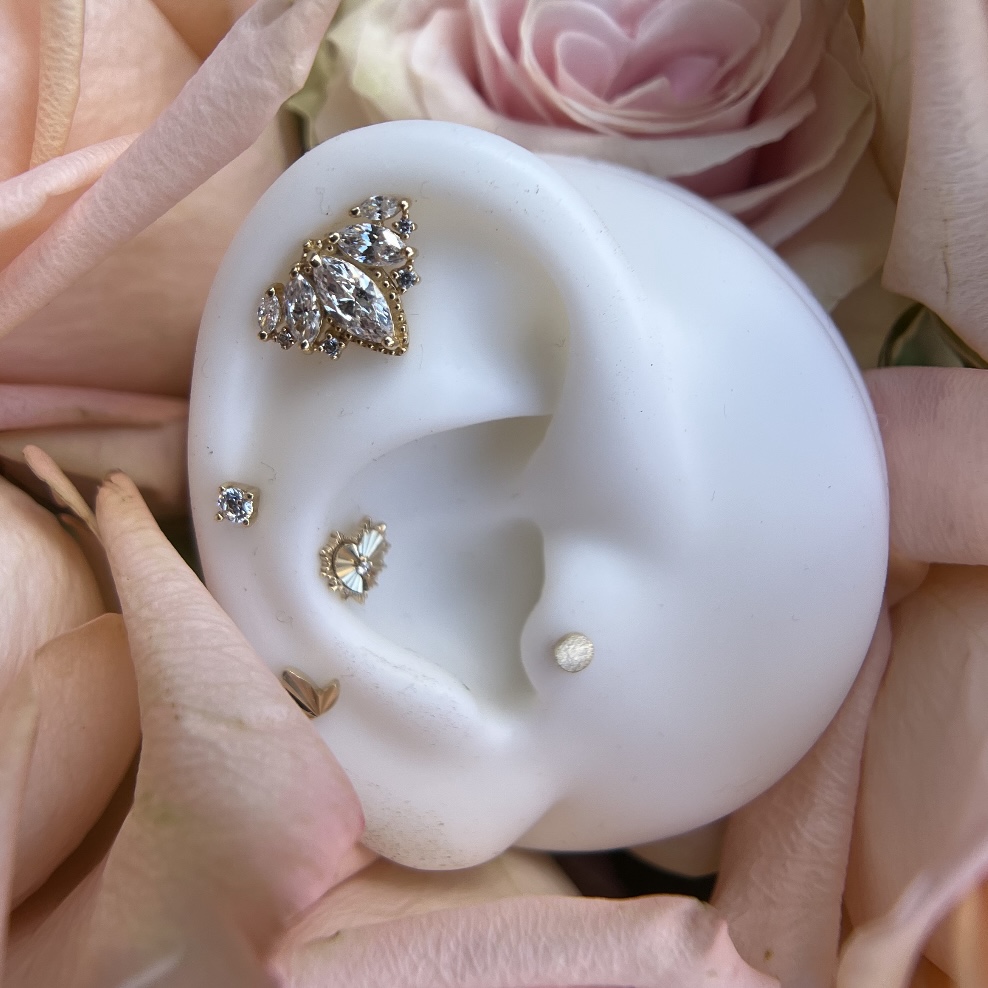 Display of various earrings on a white ear-shaped stand, with pink and peach flowers in the background.
